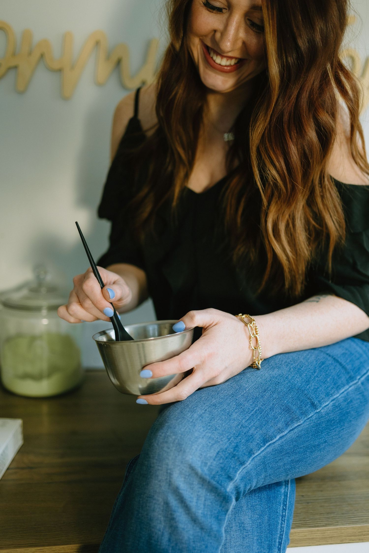 Person in black top and jeans stirring a beverage in metal cup.