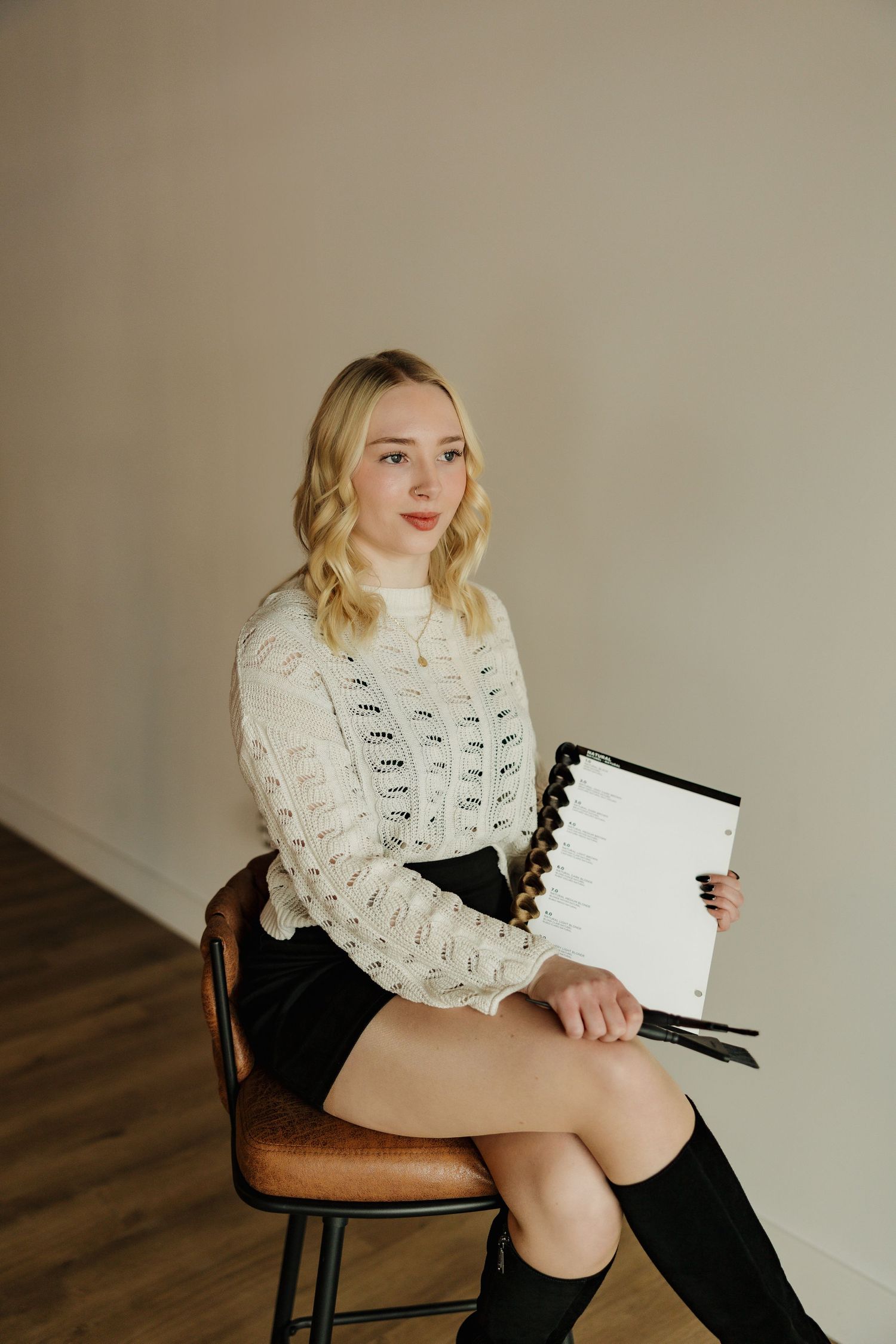 Professional headshot in white cable knit sweater holding notebook against neutral background.