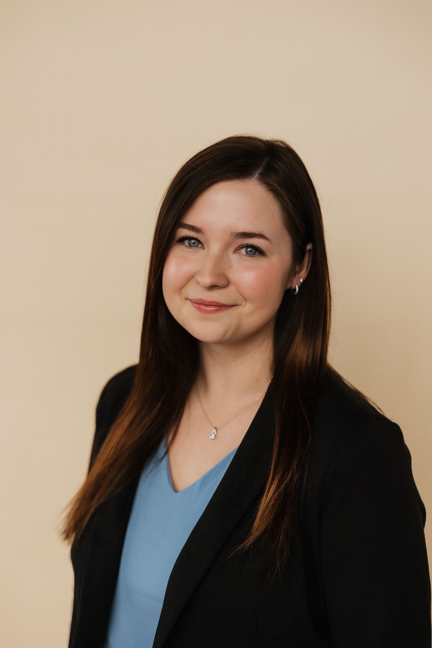 Professional portrait of person wearing black blazer and blue top against neutral background.