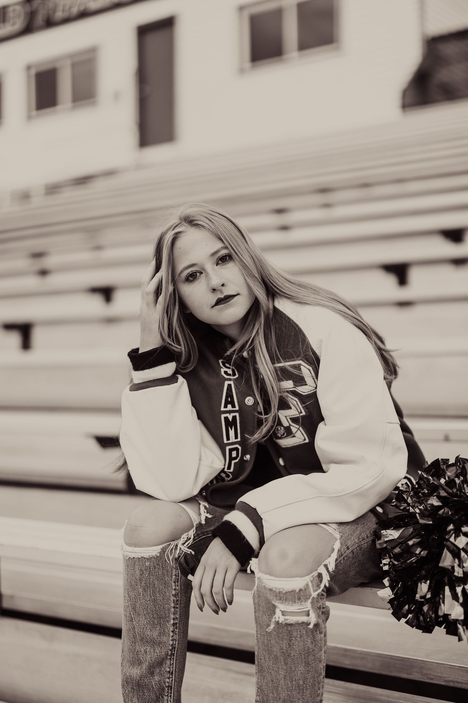 Black and white portrait of person in varsity jacket sitting on bleachers.