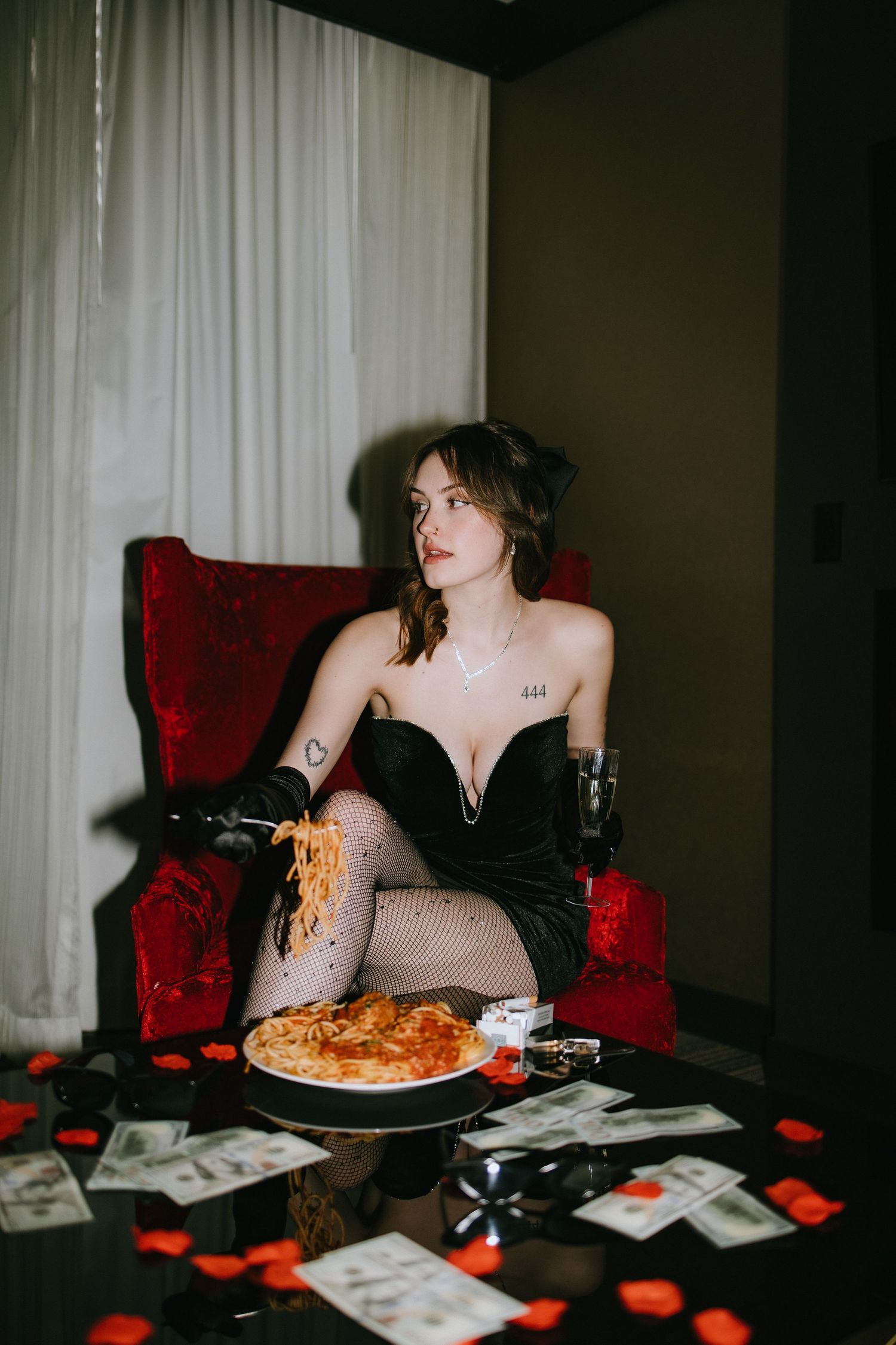 Moody boudoir scene with spaghetti dinner on red velvet chair surrounded by playing cards.