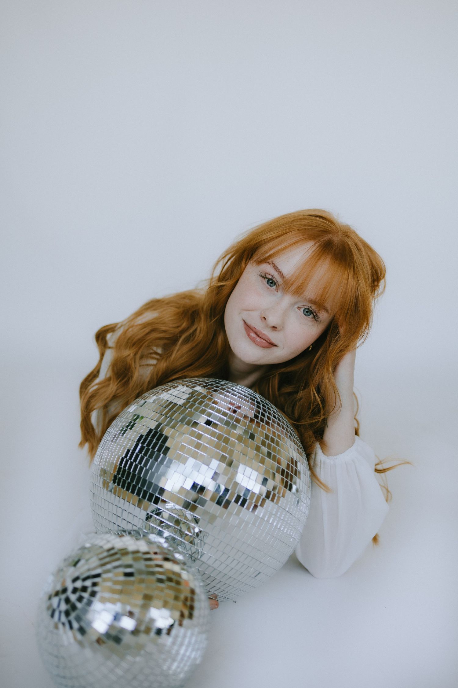 Studio portrait with disco balls and white sweater against light background.