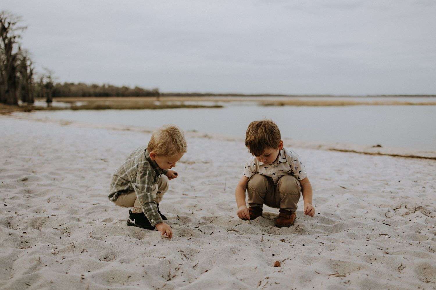 Two children playing and exploring together on a sandy beach.