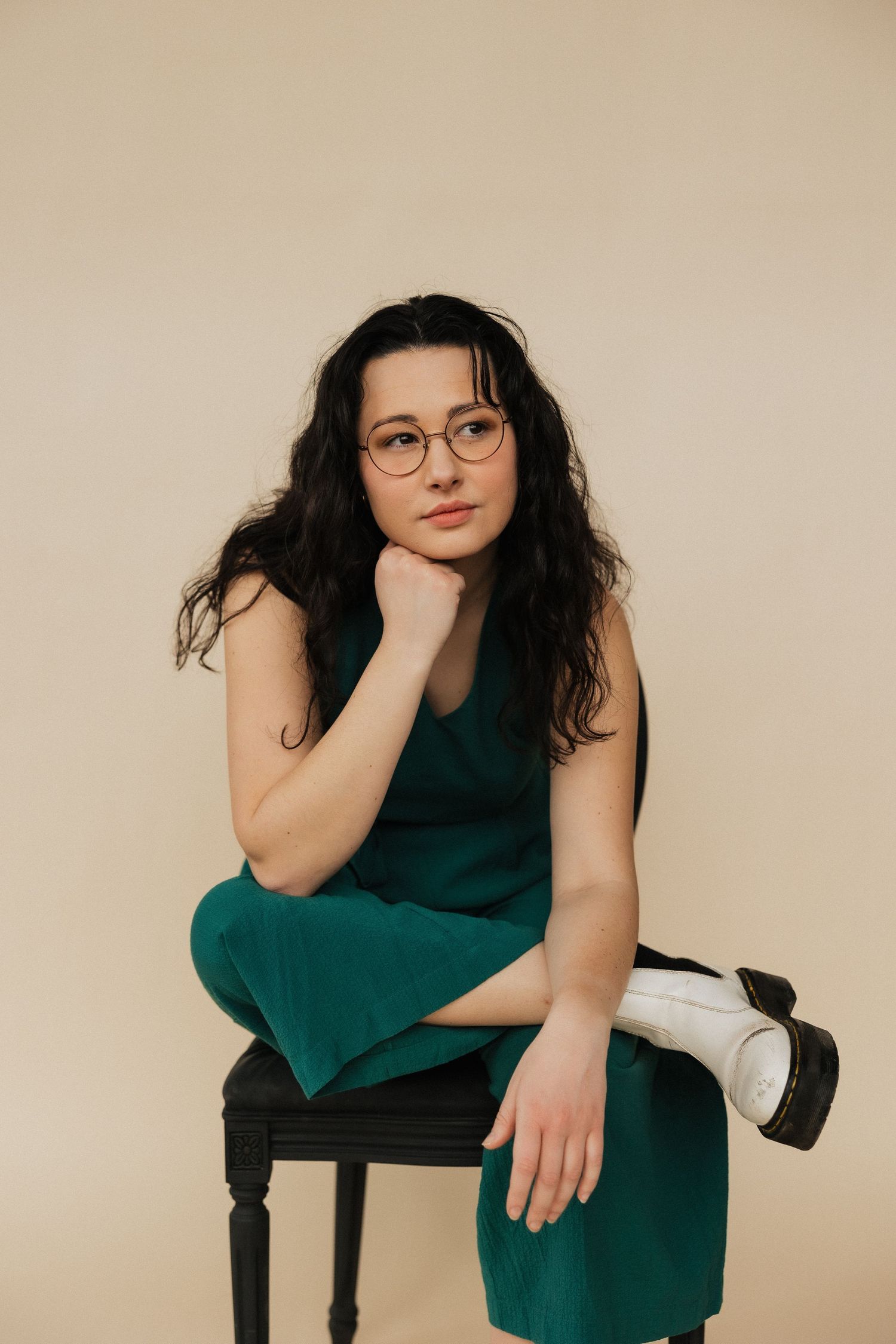 Stylish portrait of person in green dress and glasses seated on black chair.