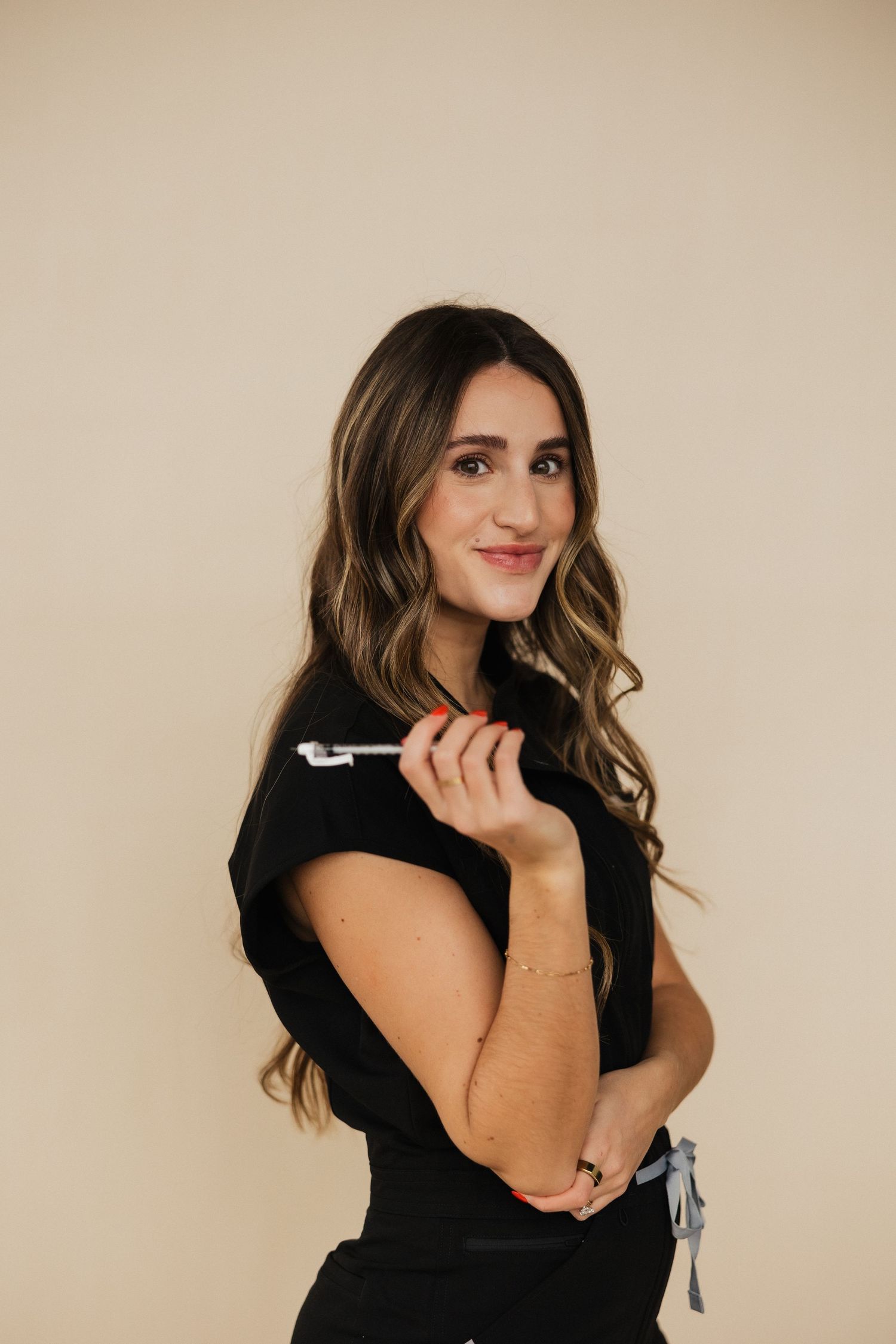 Stylish woman in black attire poses confidently with pen against neutral background.