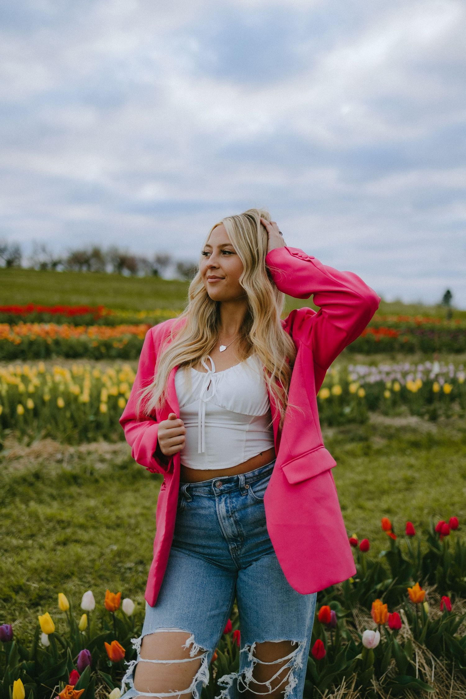 Stylish spring outfit with hot pink blazer and ripped jeans in tulip field.