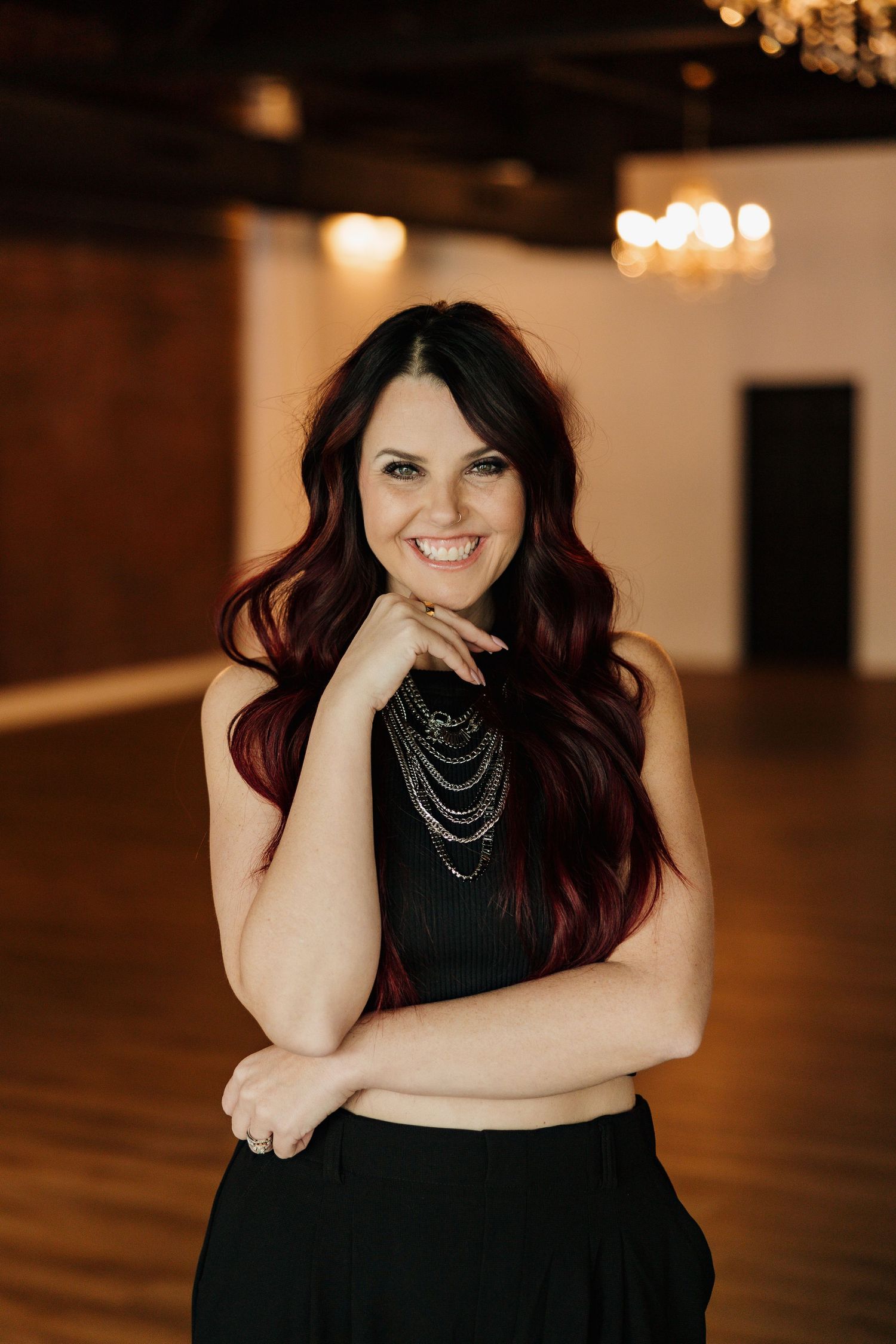 Professional portrait in a black dress with layered necklaces in an elegant venue setting.