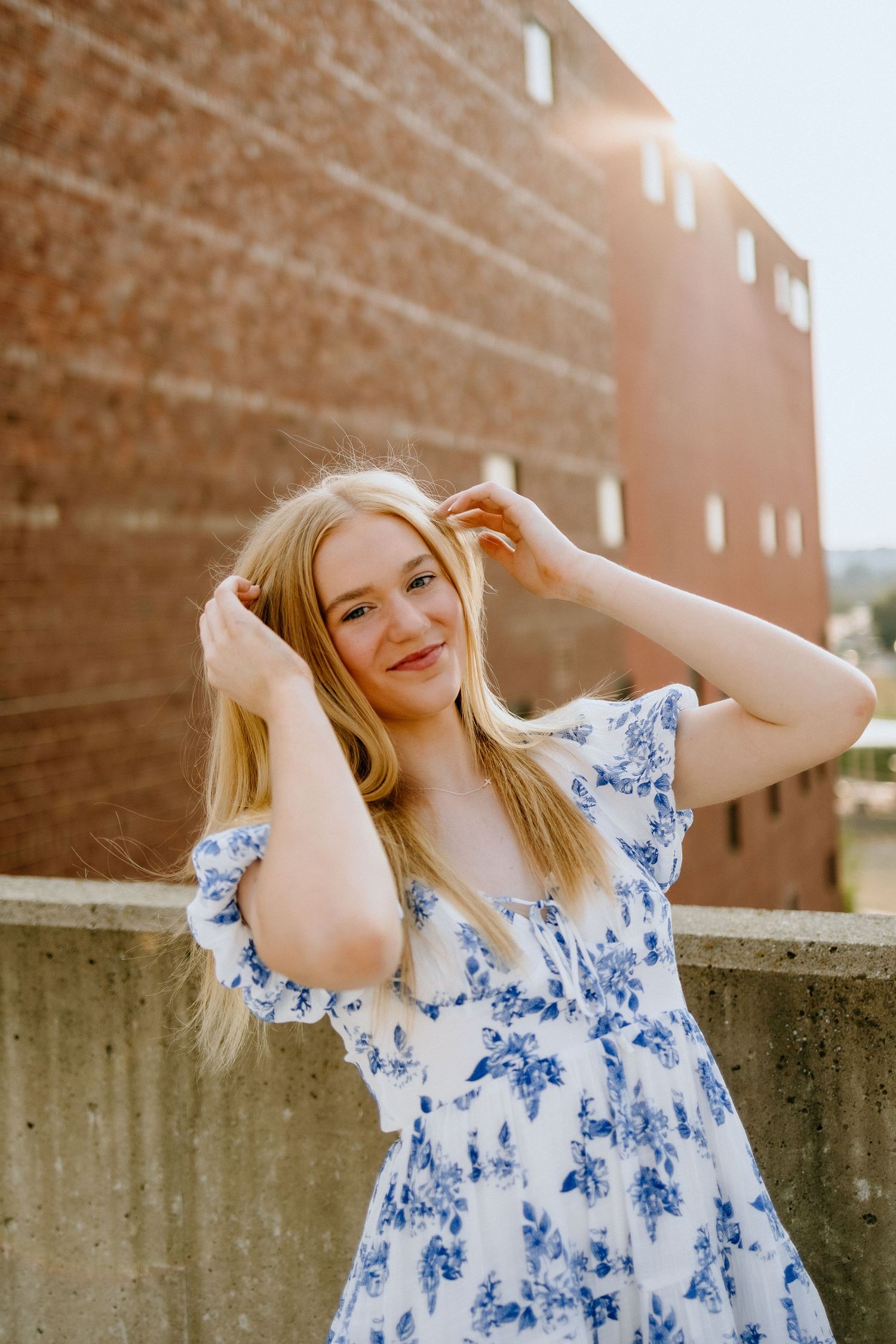 Portrait of woman in blue and white floral dress against industrial brick backdrop.