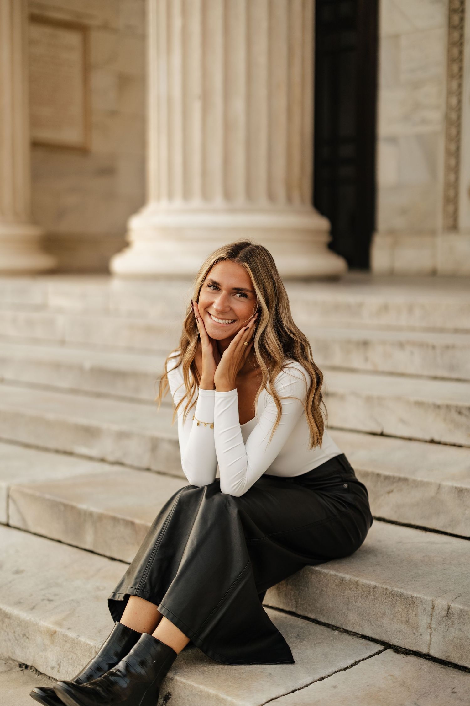 A casual portrait on marble steps features someone in a white top and black skirt sitting by classic columns.