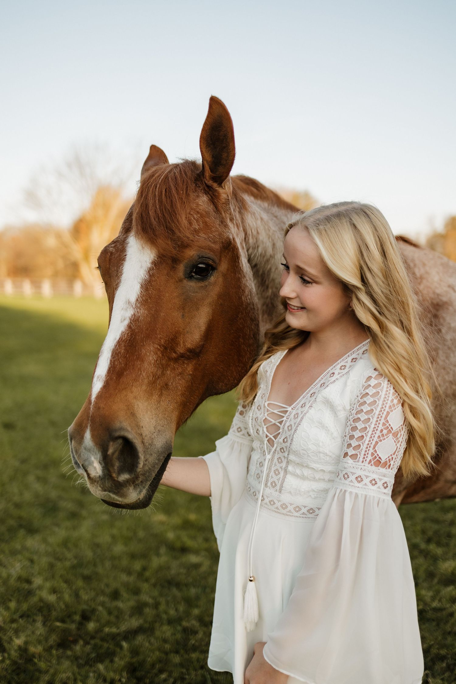 A gentle moment between a chestnut horse and someone in a white lace dress at sunset.