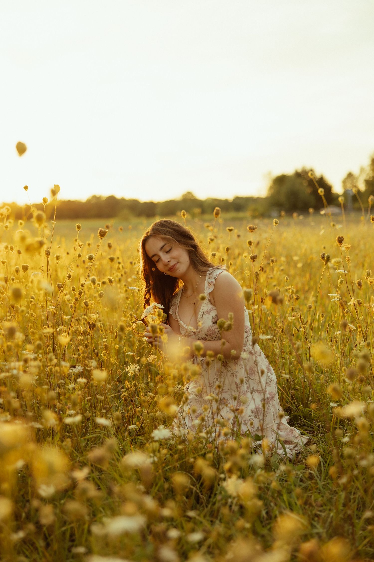 Person in white dress sitting among golden wildflowers during sunset in a dreamy summer meadow.