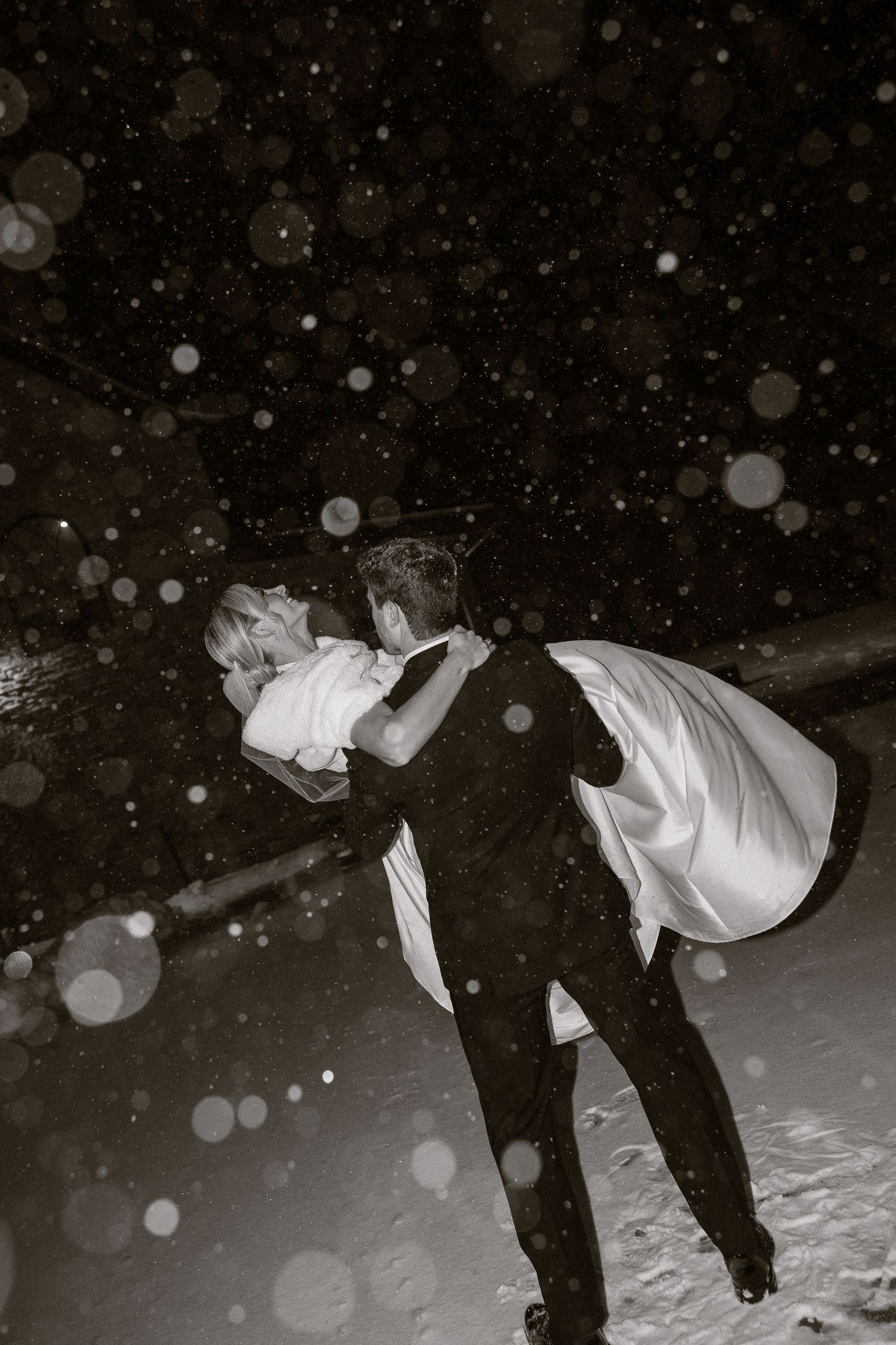 Wedding guests playing in the snow at night with snowflakes falling.