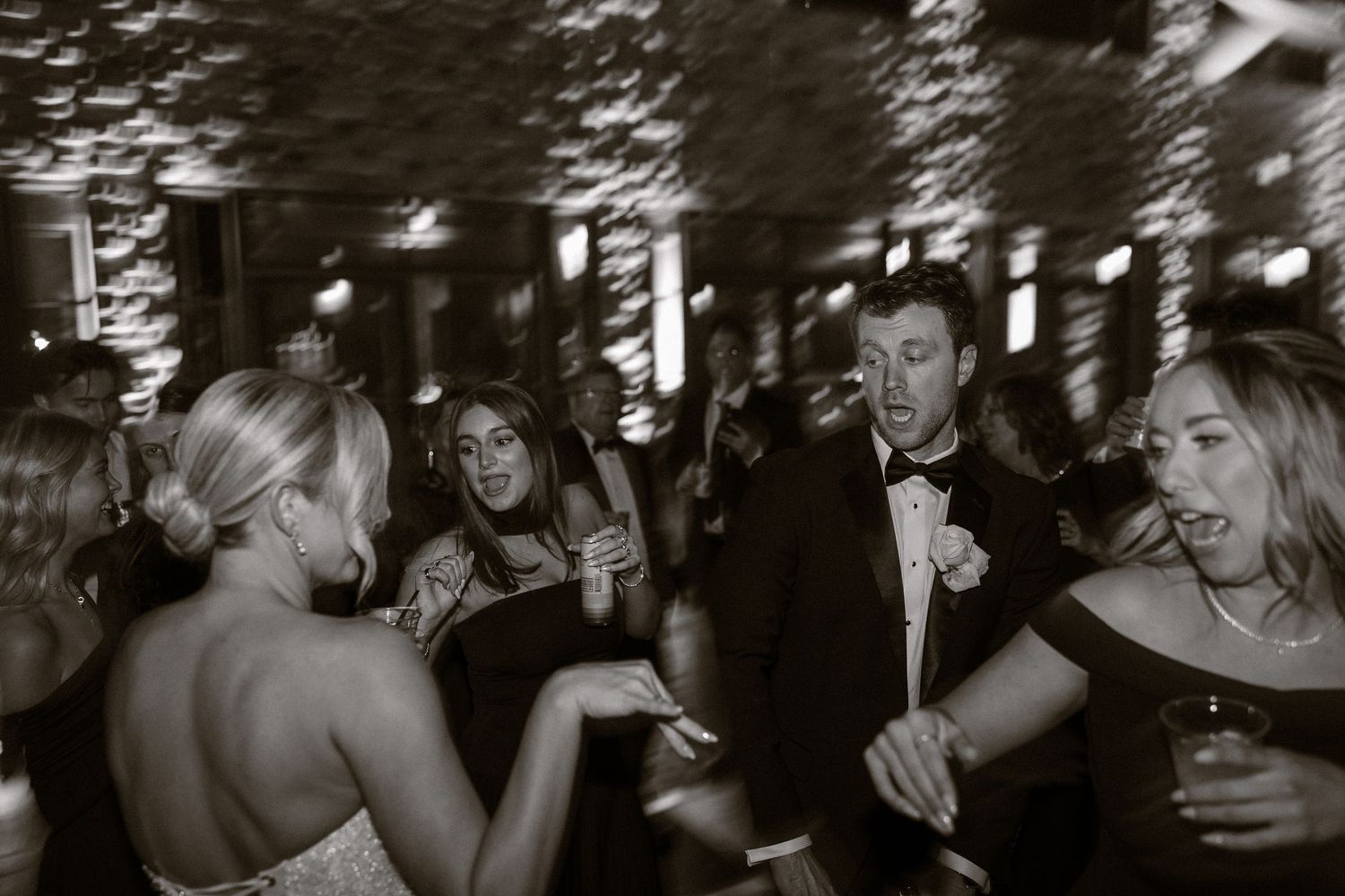Wedding reception guests dancing and celebrating in a dimly lit venue.