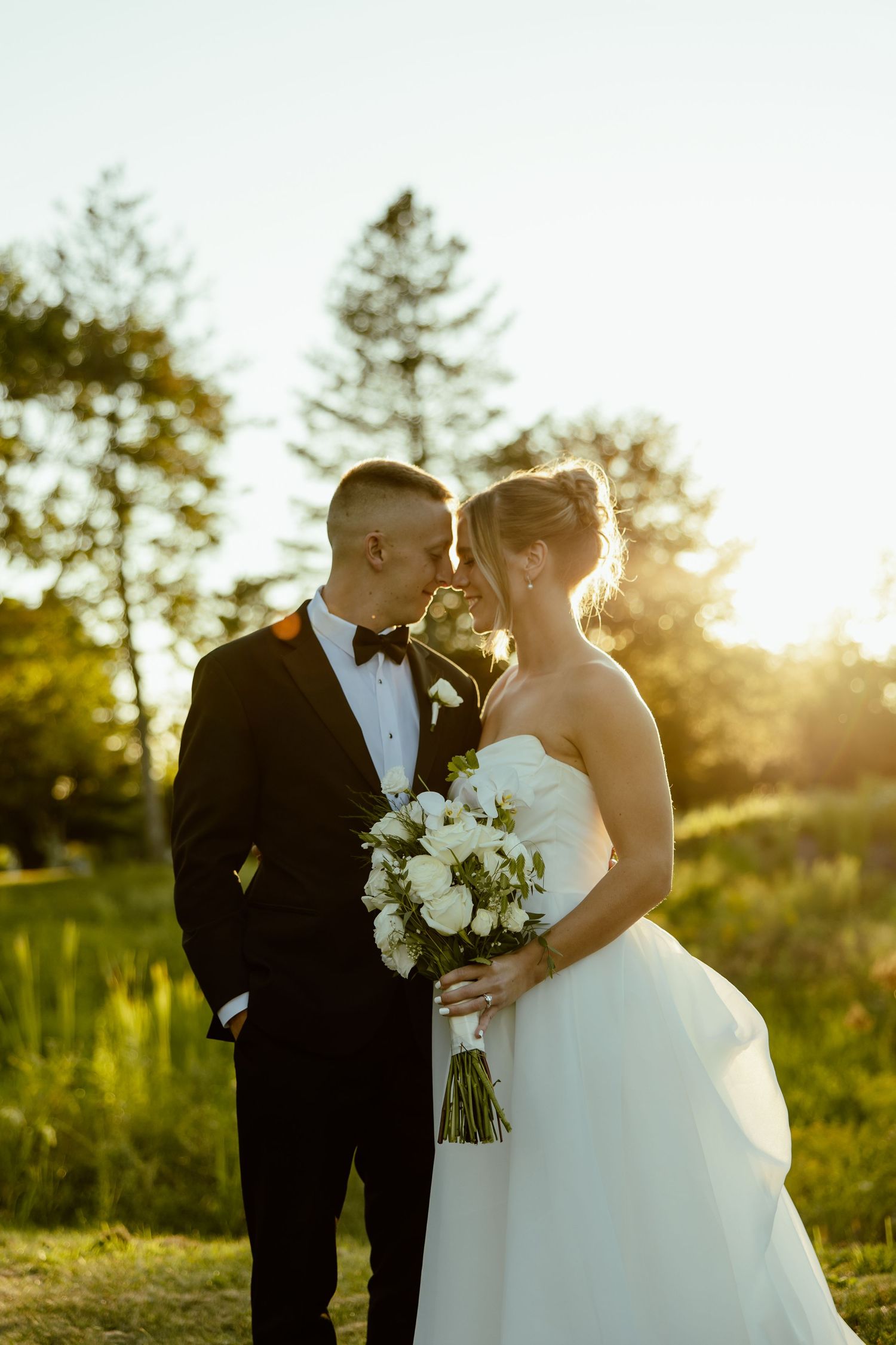 A romantic sunset wedding photo of a couple with white bouquet in an outdoor setting.