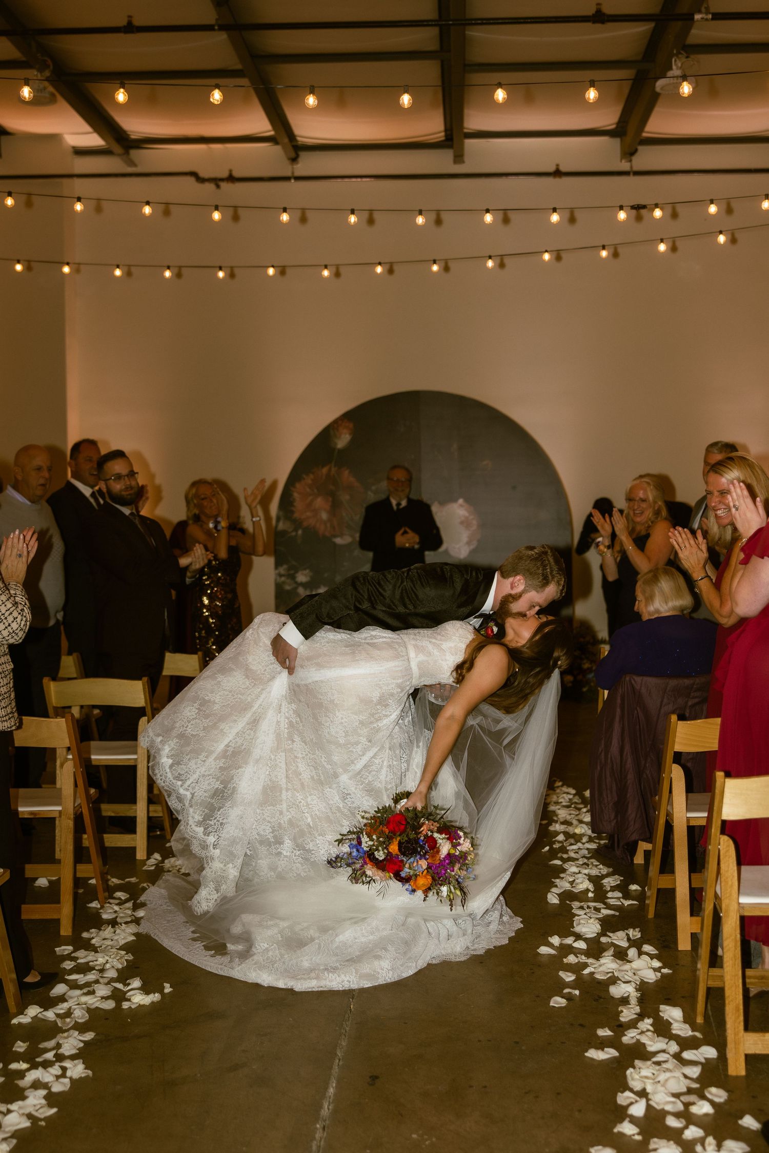 Wedding reception sequence showing dancing and twirling on a floor decorated with rose petals under string lights.