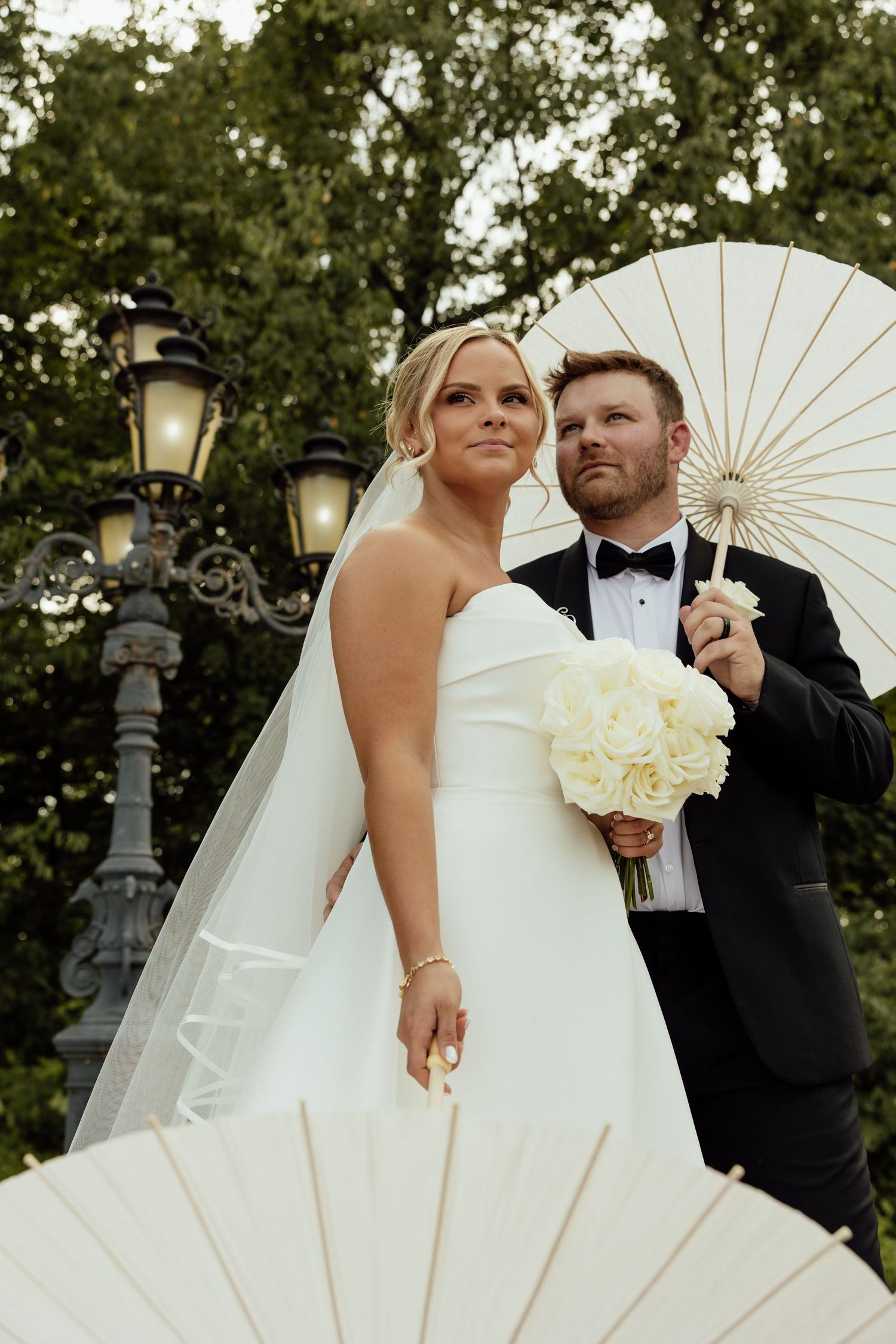 A bride in a voluminous white gown poses with a parasol during outdoor wedding portraits.