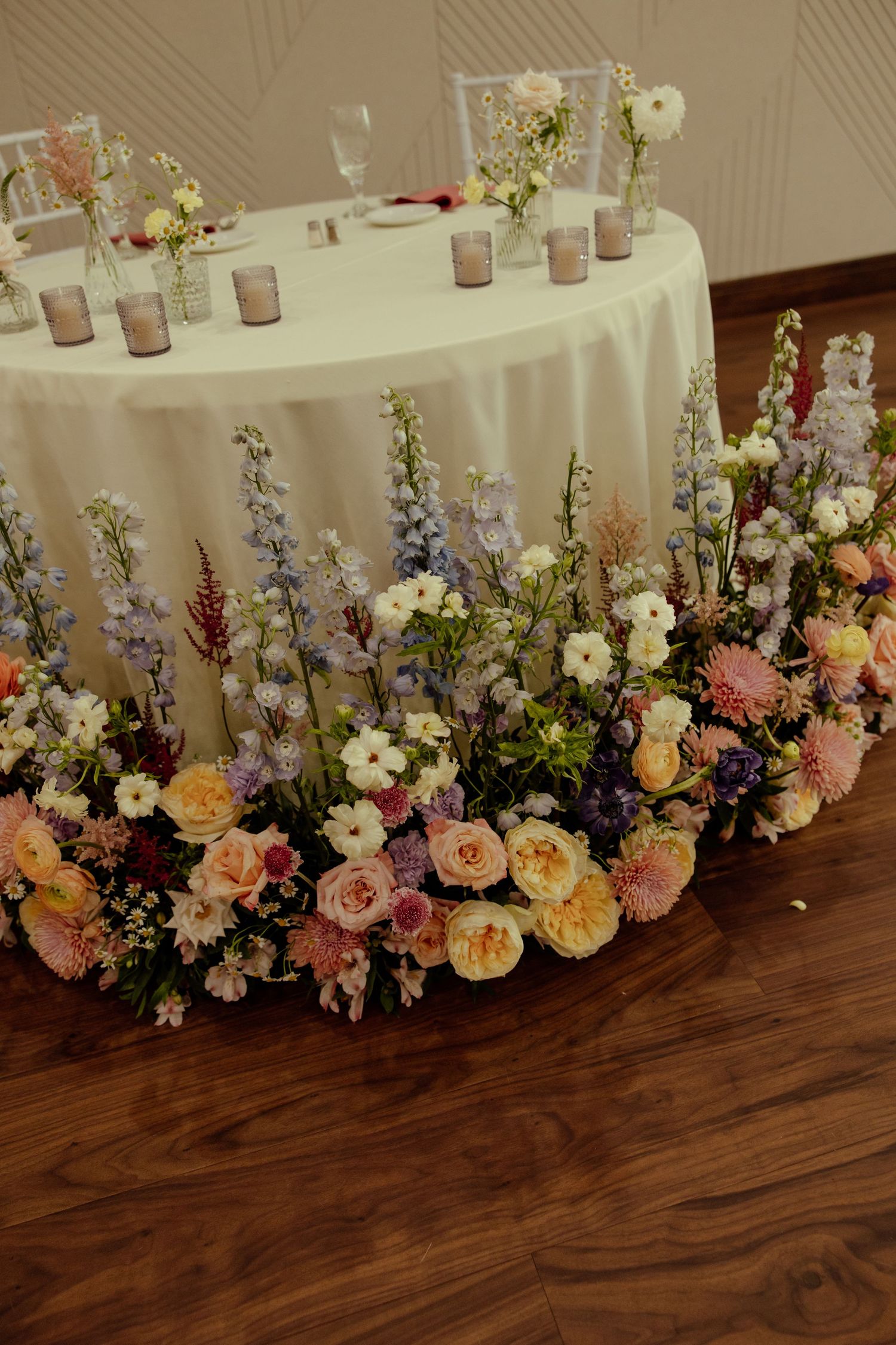Elegant floral arrangements with pink and white roses line a wooden floor against a white backdrop.