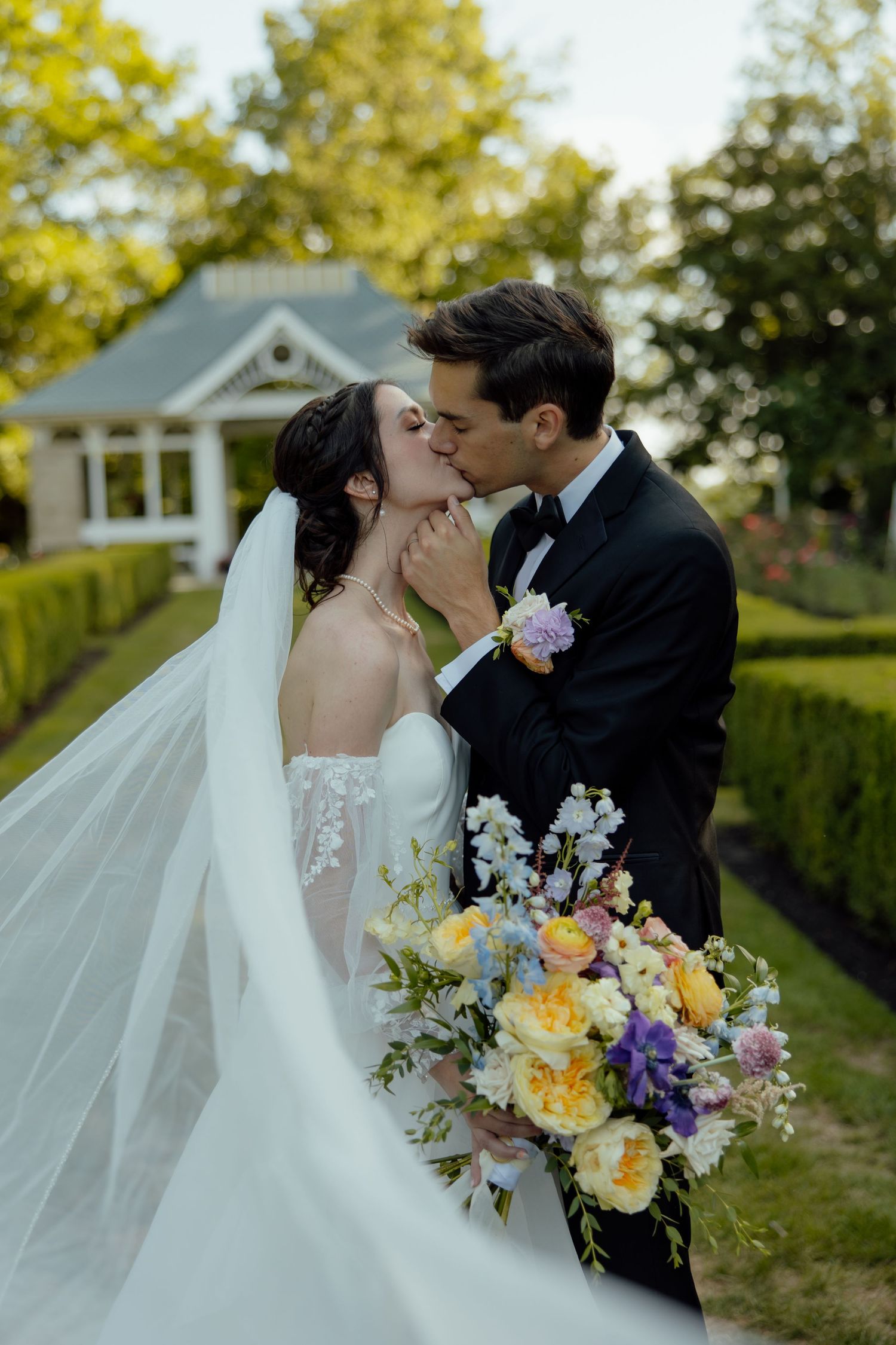 Romantic wedding portrait with flowing veil and colorful bouquet in a garden setting.