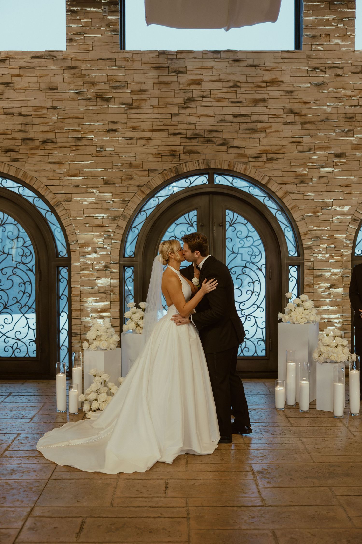 Couple shares an intimate moment in an elegant stone venue with arched windows and candles.