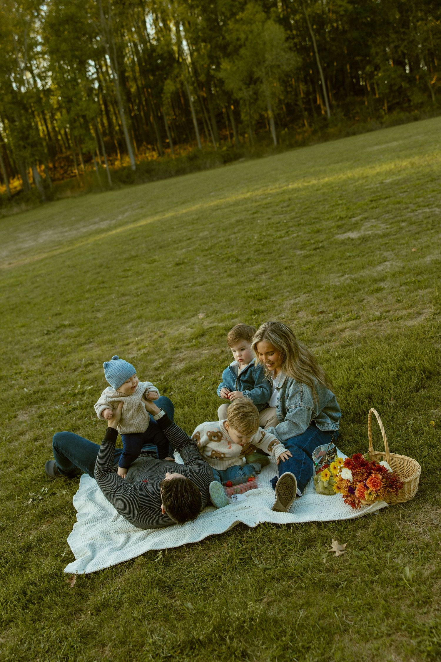 Family enjoying a picnic on a blanket in a grassy field during golden hour.