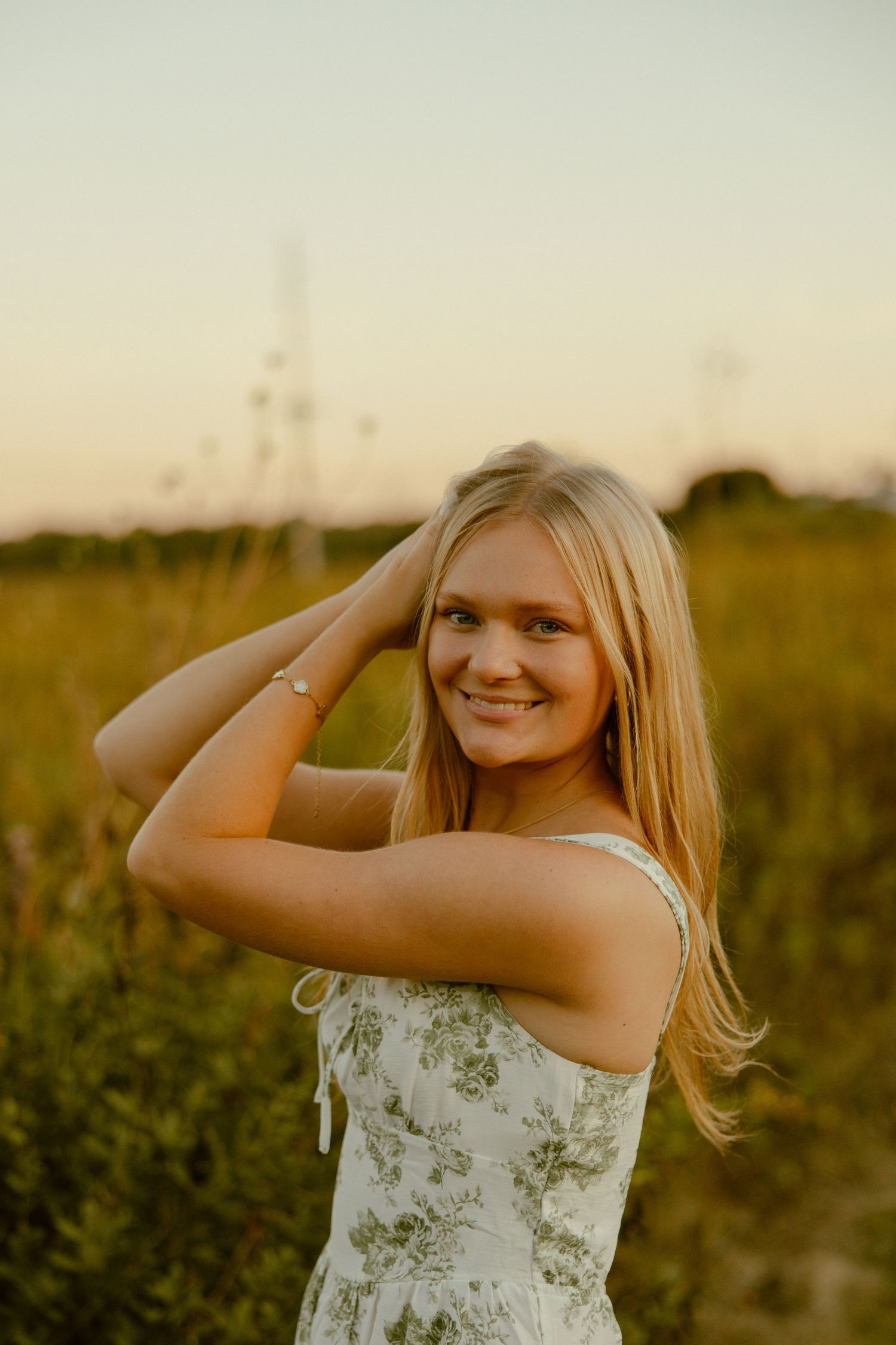 A person in a floral sundress poses in a golden field at sunset with a warm summer glow.
