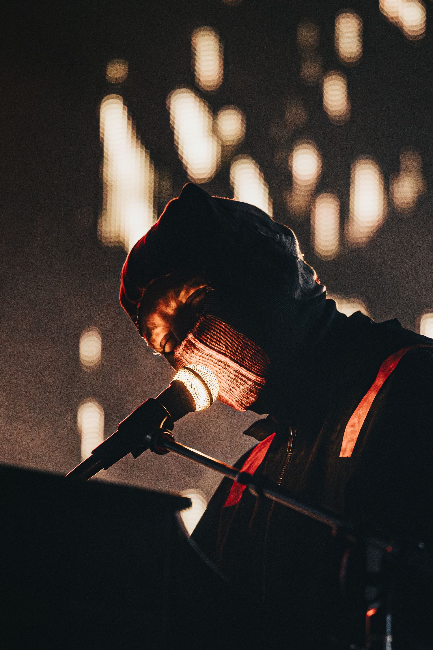 Close-up silhouette of performer with microphone against warm bokeh lighting.