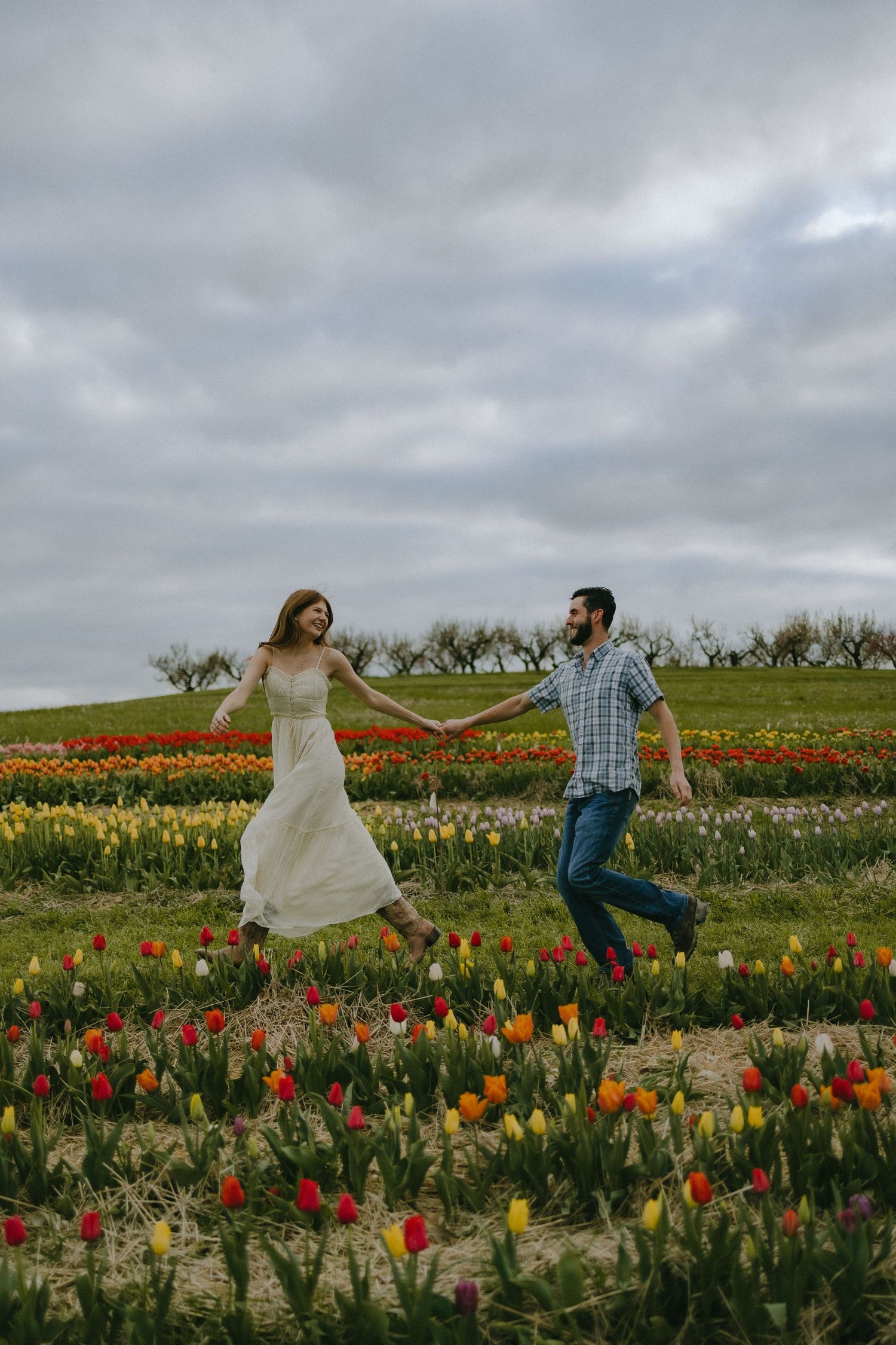 A joyful couple jumping in a colorful tulip field under cloudy skies.