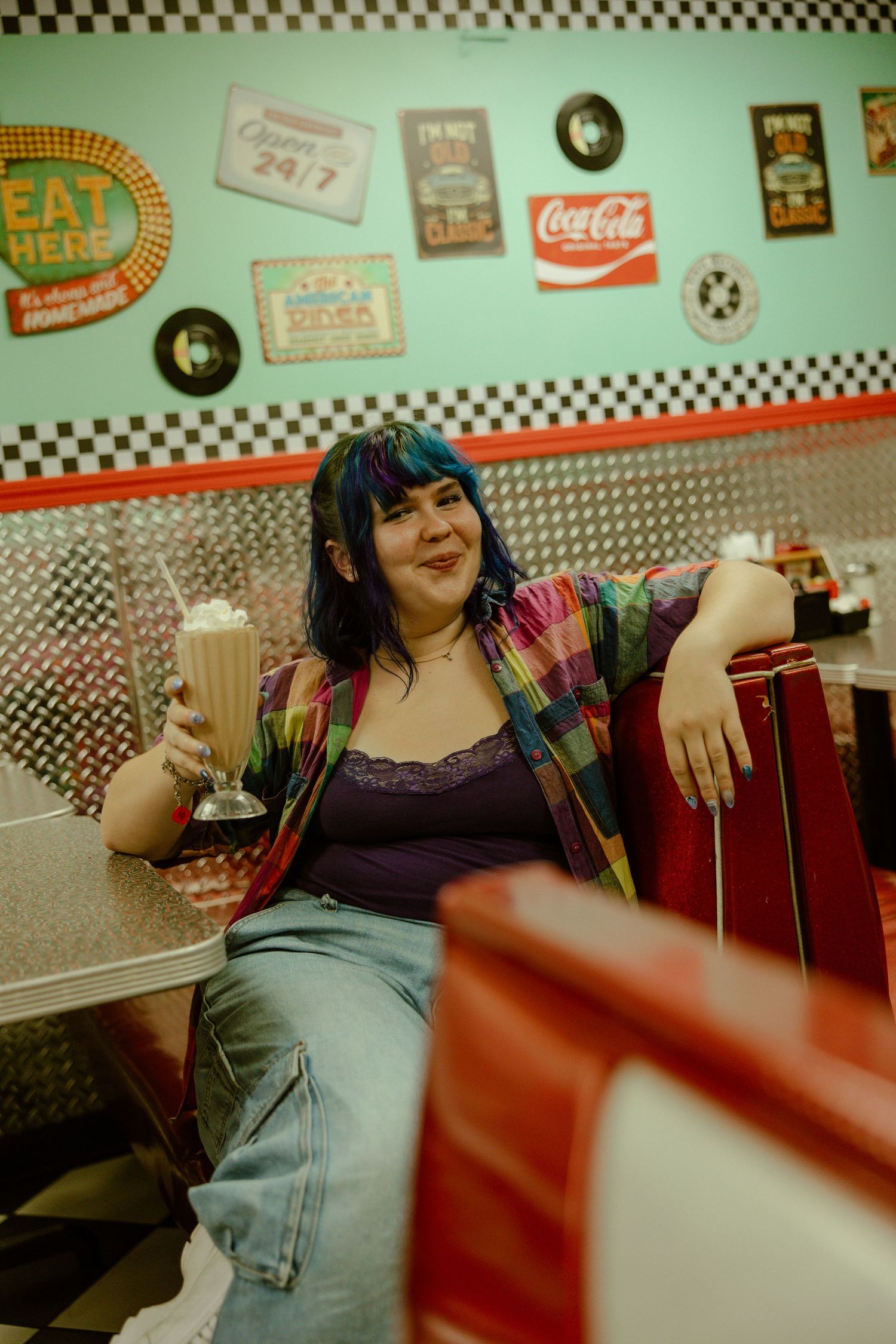 A retro-style diner interior with checkered borders and vintage Coca-Cola signs decorating the walls.