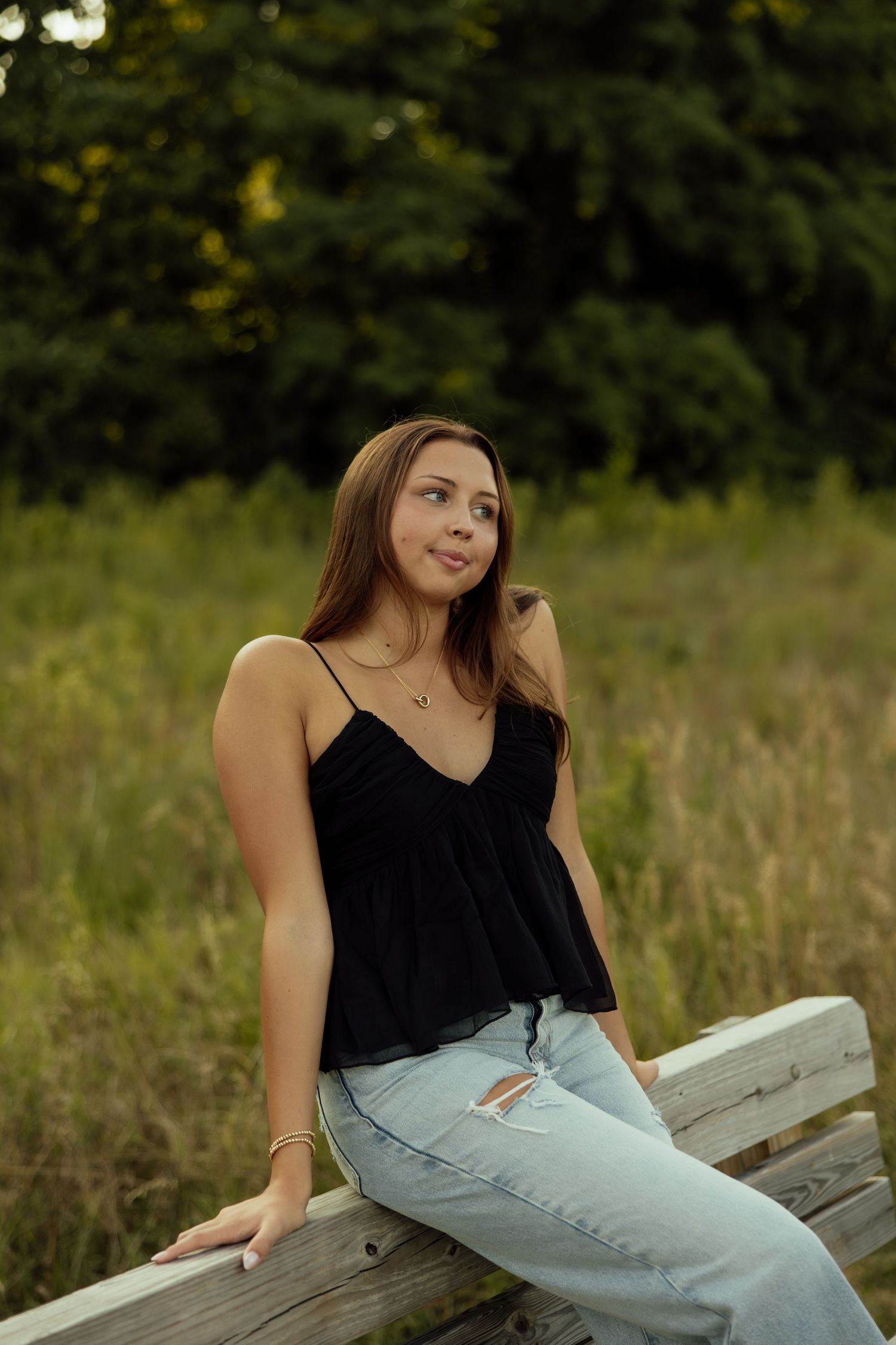 A person in a black tank top and light jeans sits casually on a wooden bench in a natural outdoor setting.