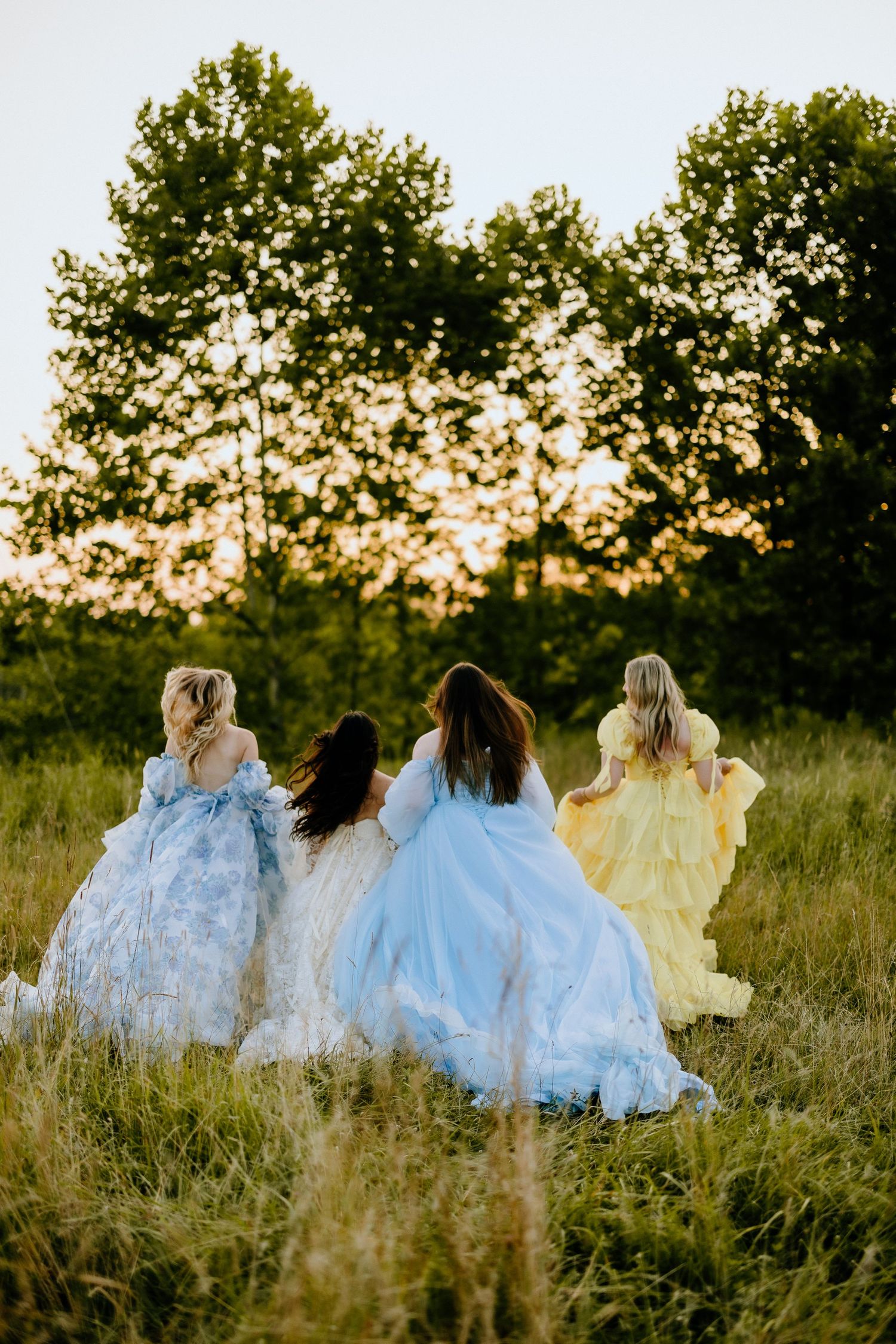 Four flowing dresses in pastel colors walking through sunset meadow.