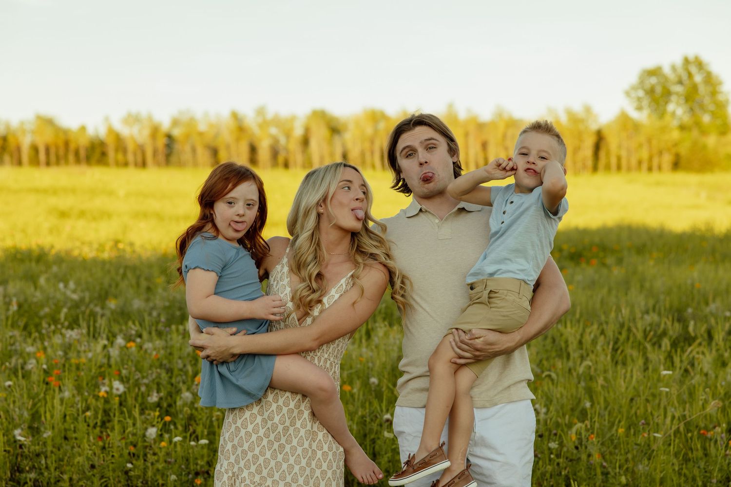 A family in casual attire embraces while standing in a sunlit meadow filled with wildflowers during golden hour.