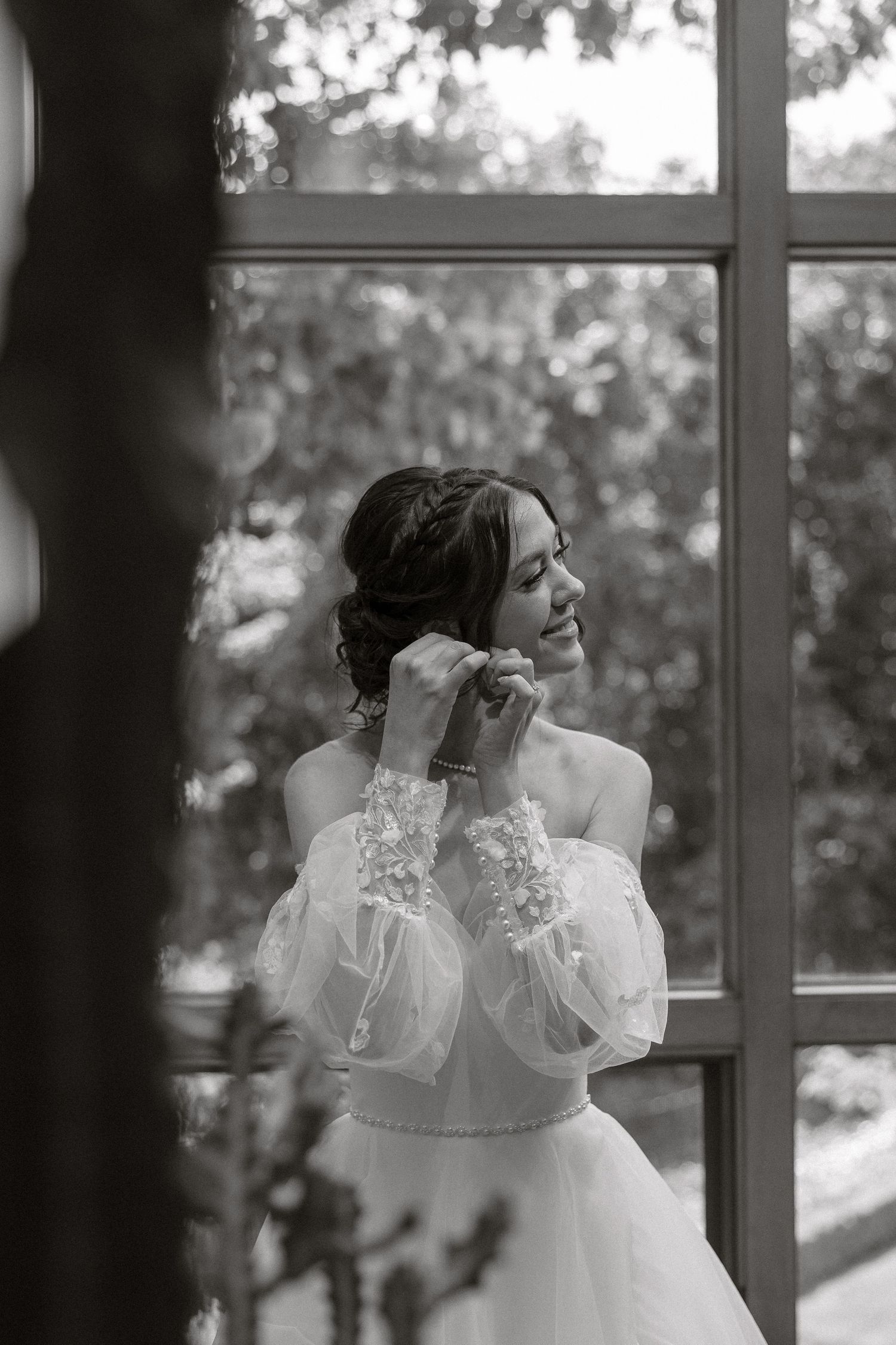 A black and white portrait shows a bride in a lace dress near windows.