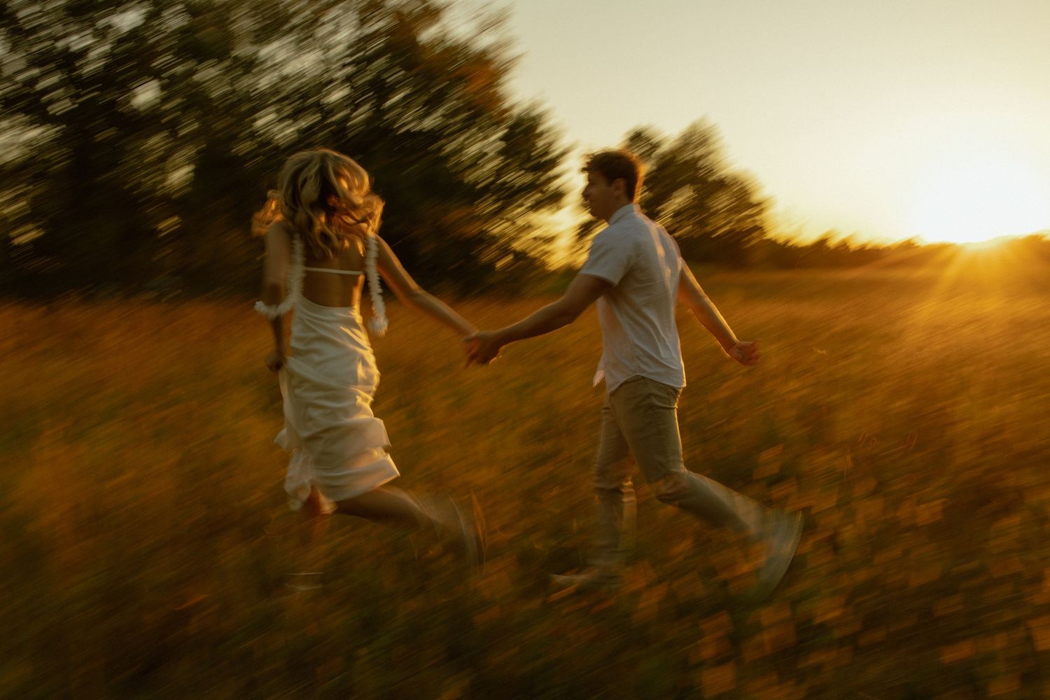 Two people hold hands while running through a golden field at sunset with motion blur effect.
