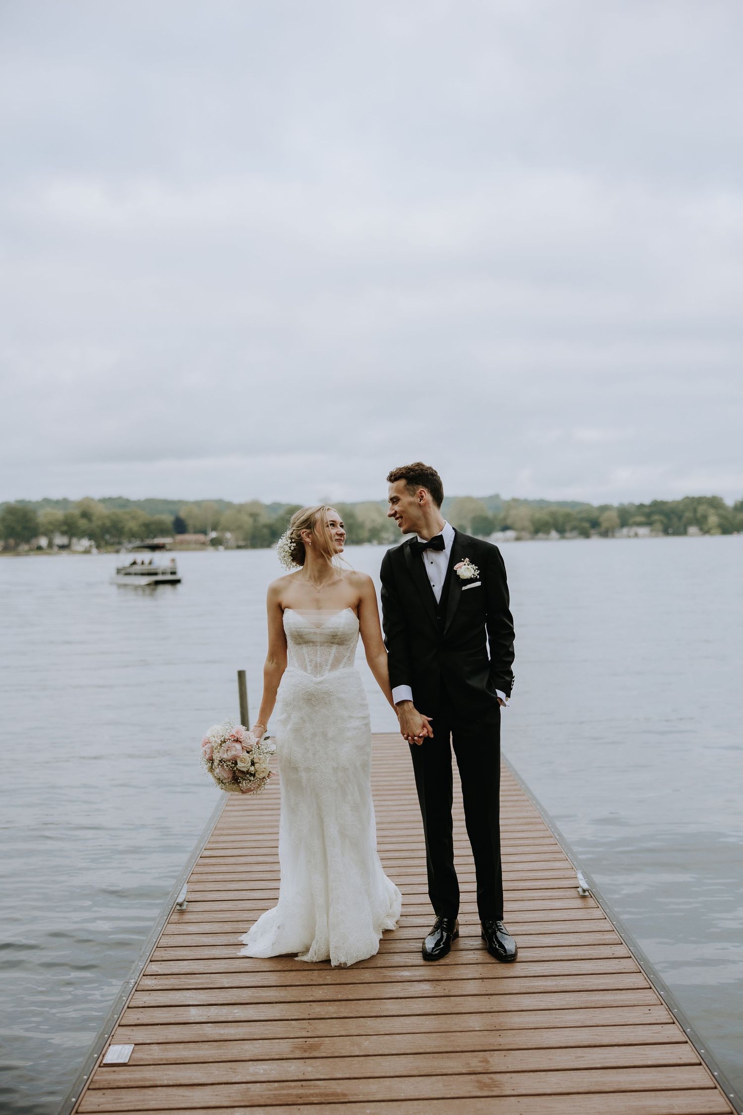 A couple shares intimate moments on a wooden dock overlooking a serene lake on their wedding day.