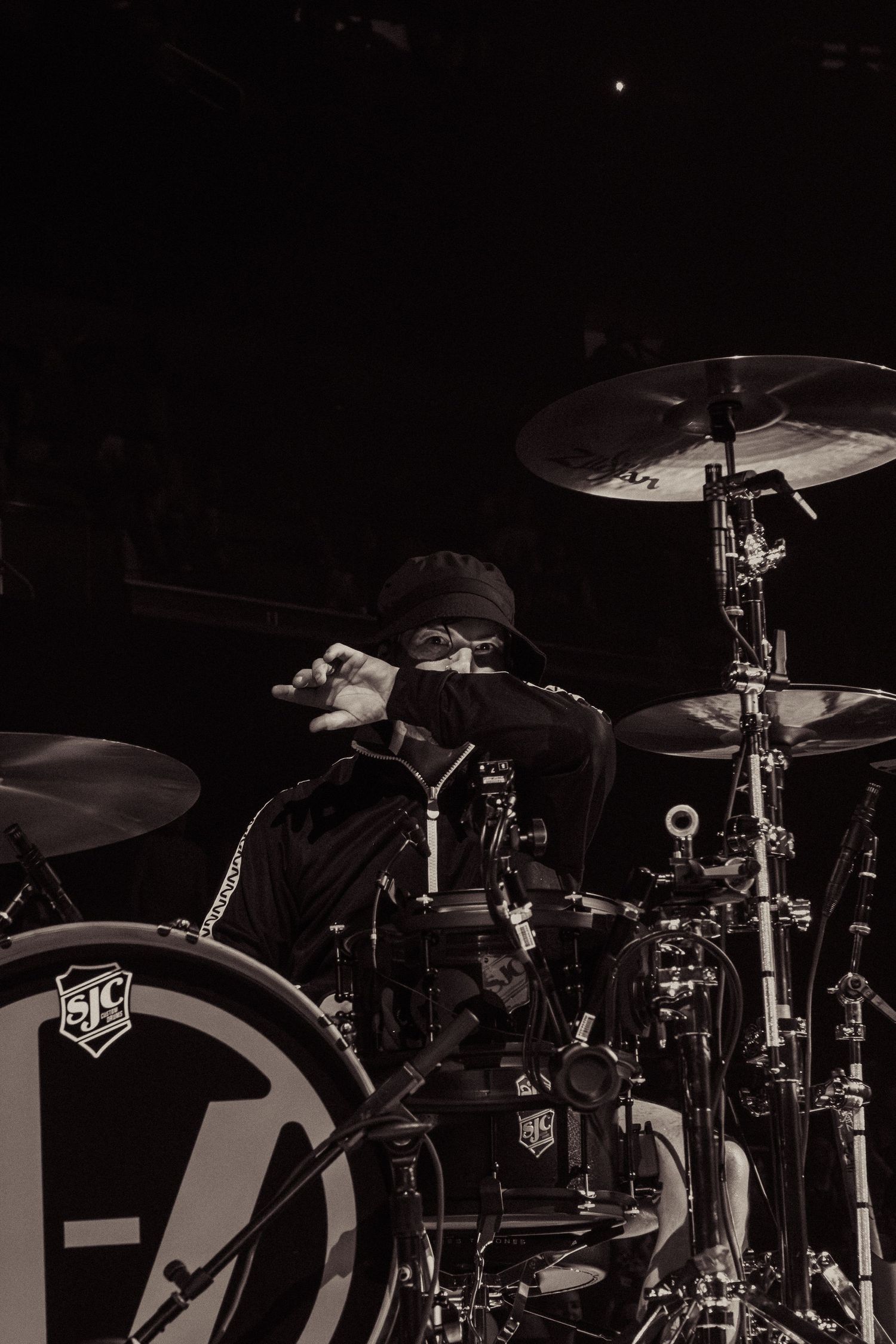 Black and white photo of drummer performing behind branded drum kit on dark stage.