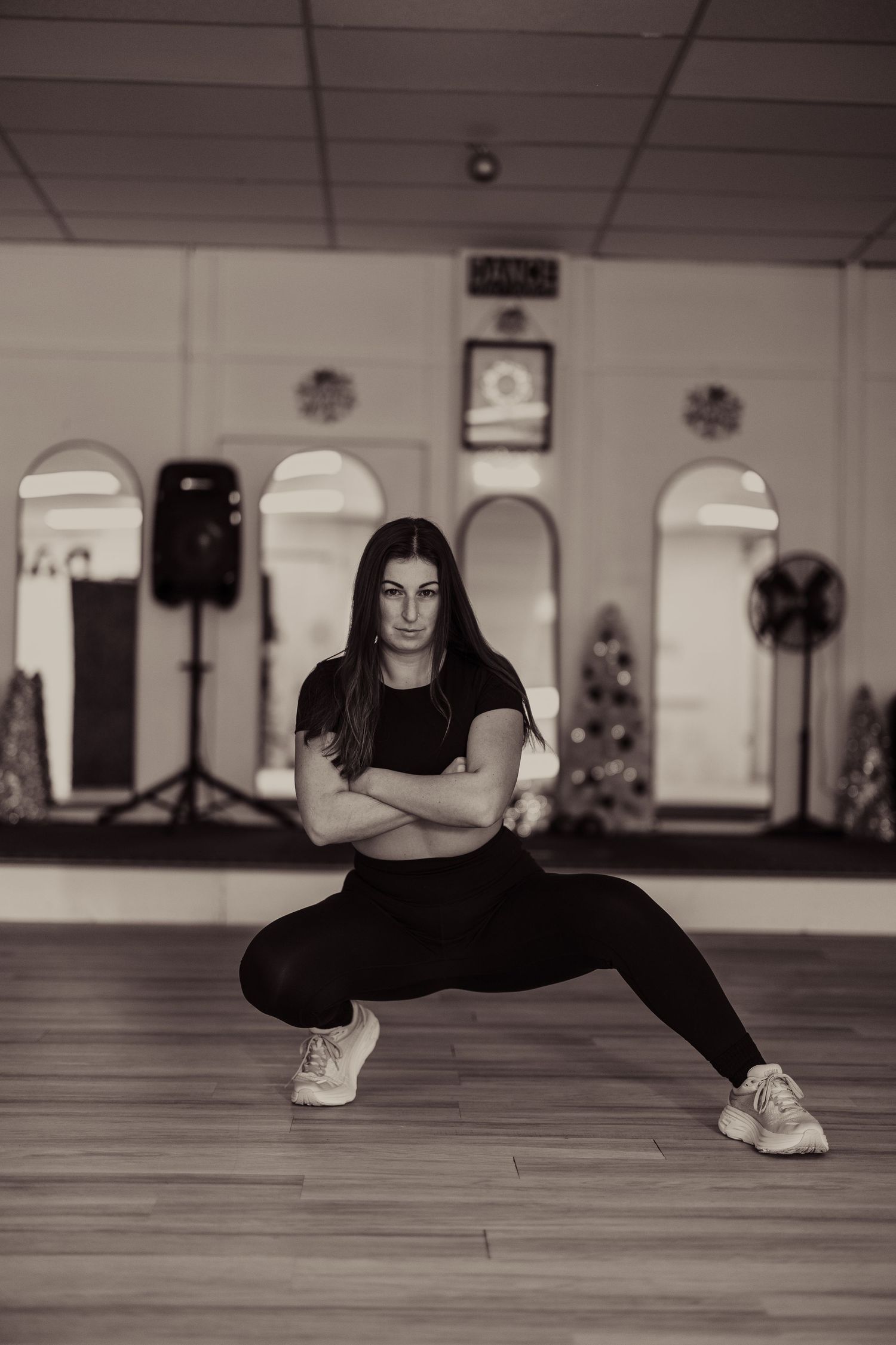 Woman performing a wide squat stance in black athletic wear inside a dance studio with arched mirrors.
