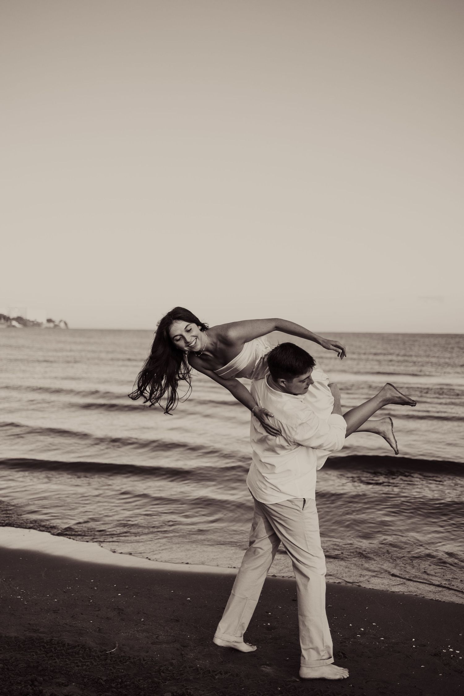 A dramatic black and white dance pose captured on a beach at sunset.