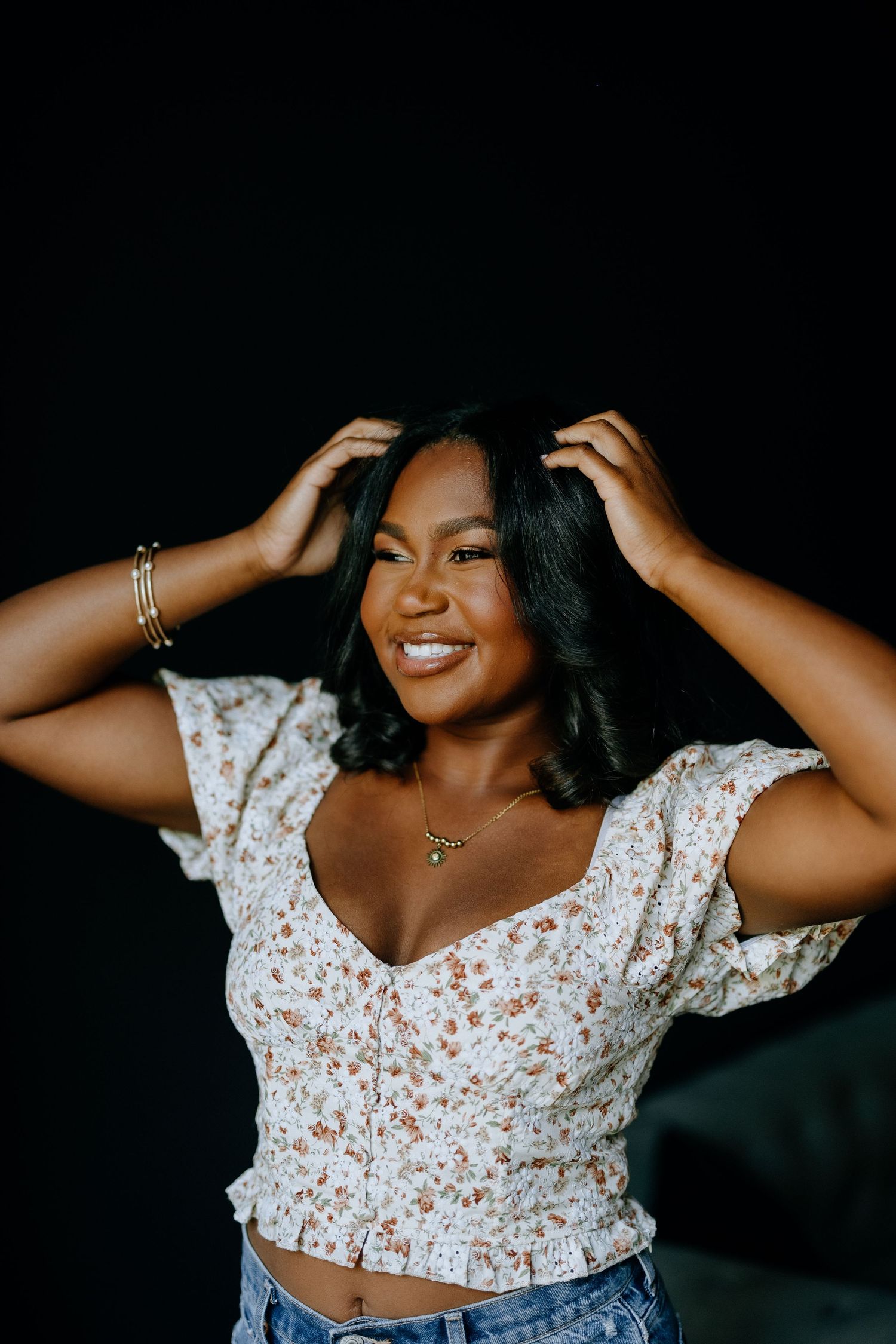 Joyful portrait in white floral top with hands in hair.