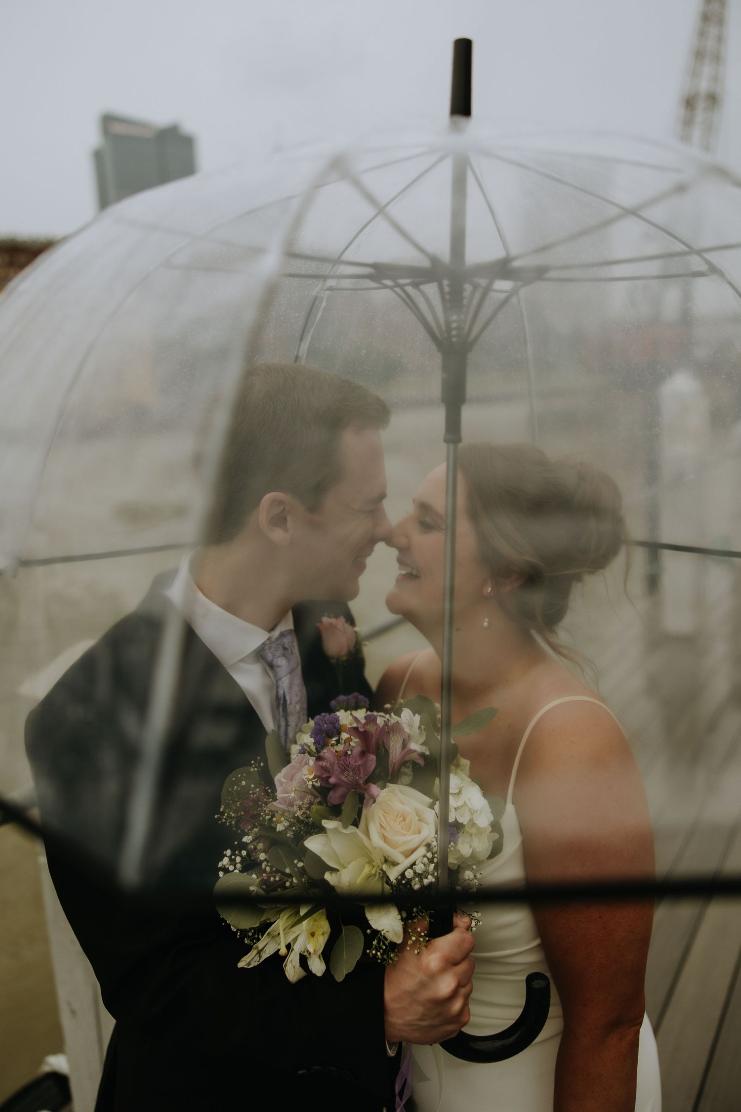 A romantic wedding moment captured through clear umbrellas in soft, dreamy lighting.