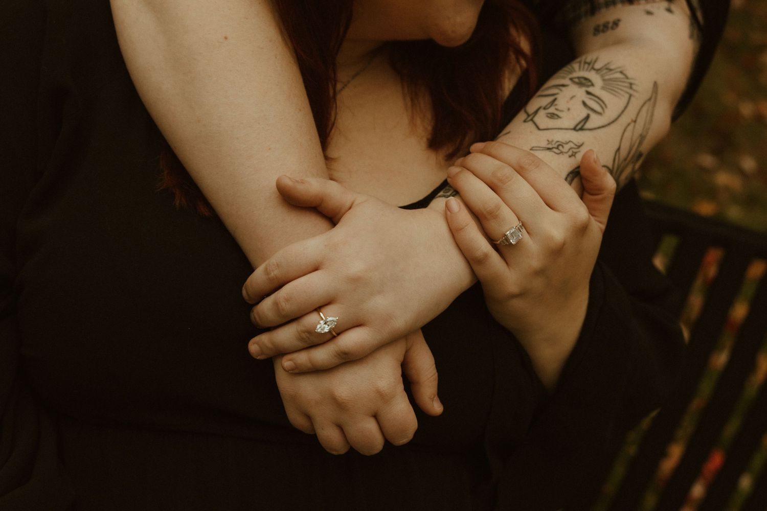 Close-up view of hands with tattoos and rings in warm moody lighting against dark background.