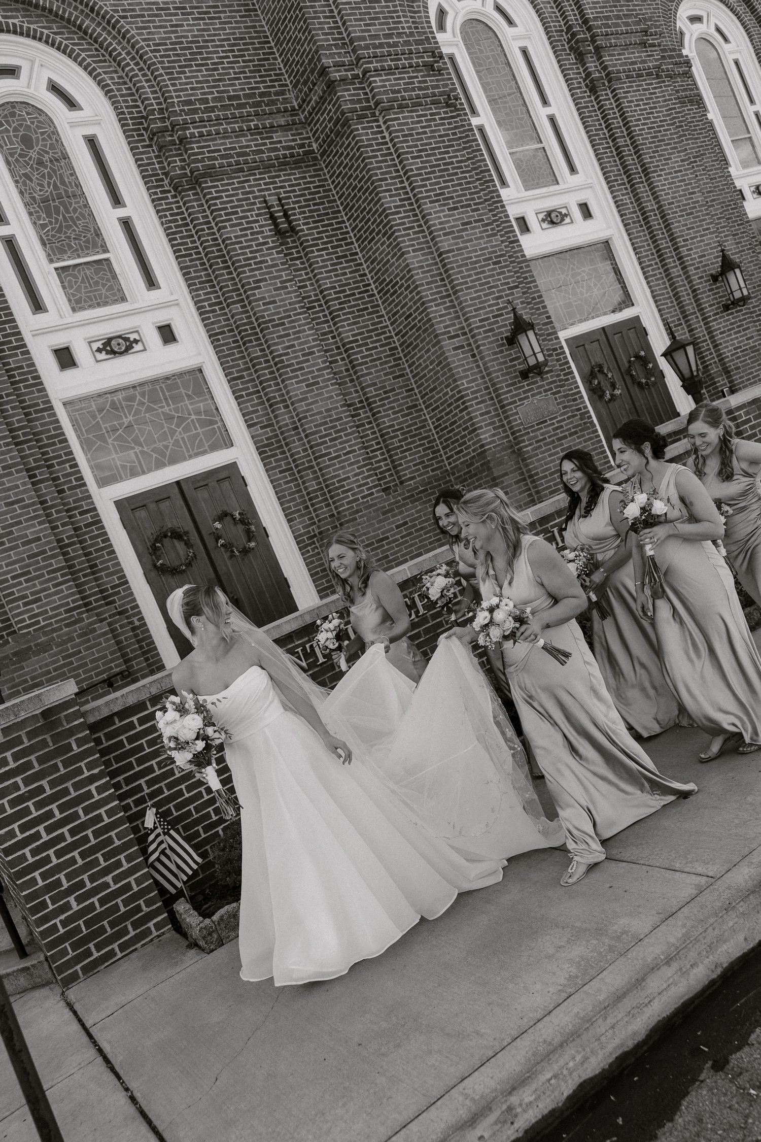 Black and white photo of bridesmaids in white dresses sitting on church steps.