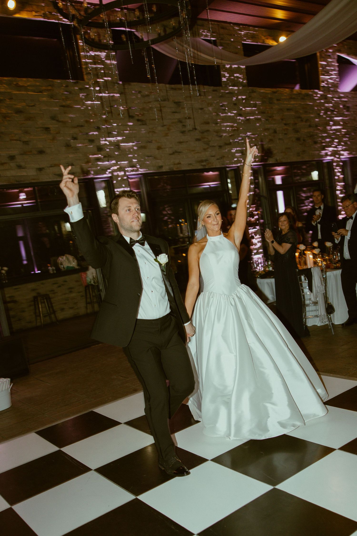 Couple performs choreographed dance moves on black and white checkered floor at reception.