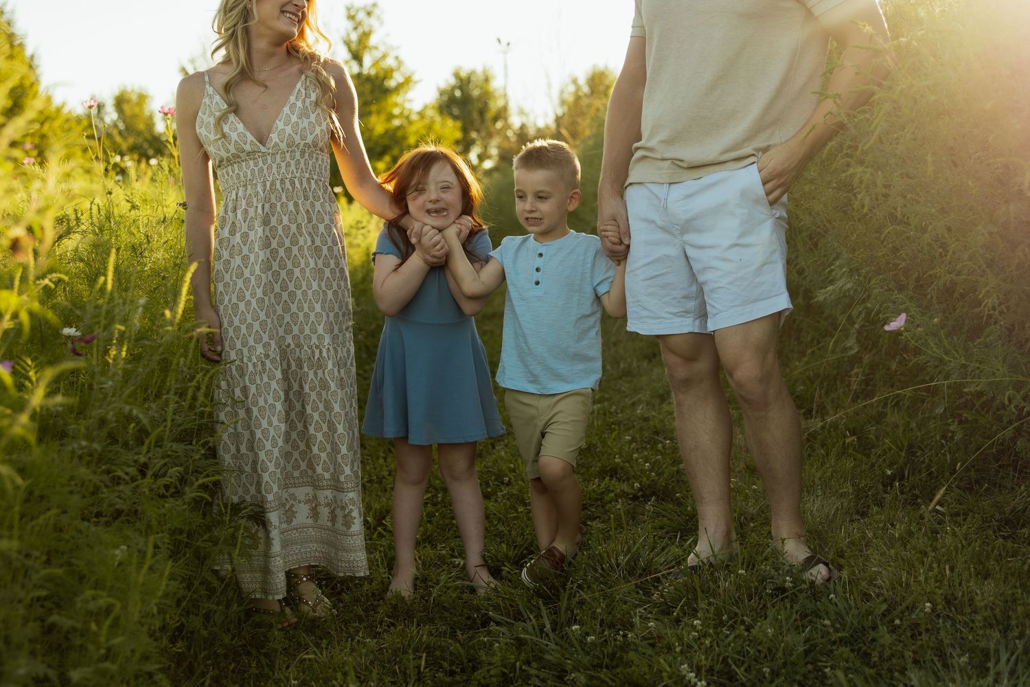 A group of people stand together in a garden during golden hour as sunlight filters through trees in the background.