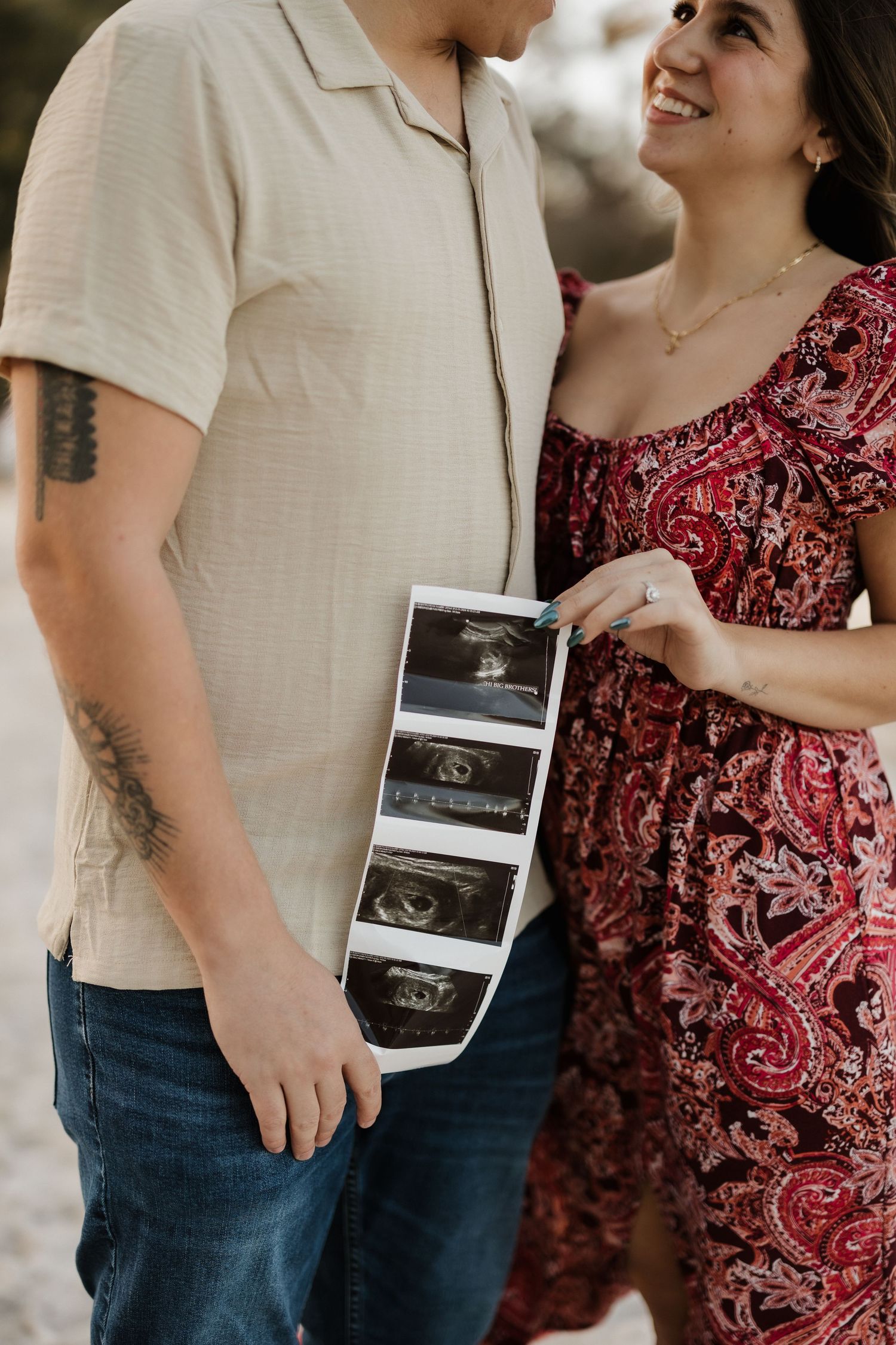 Couple in casual attire holding ultrasound strip photos while sharing loving glance.