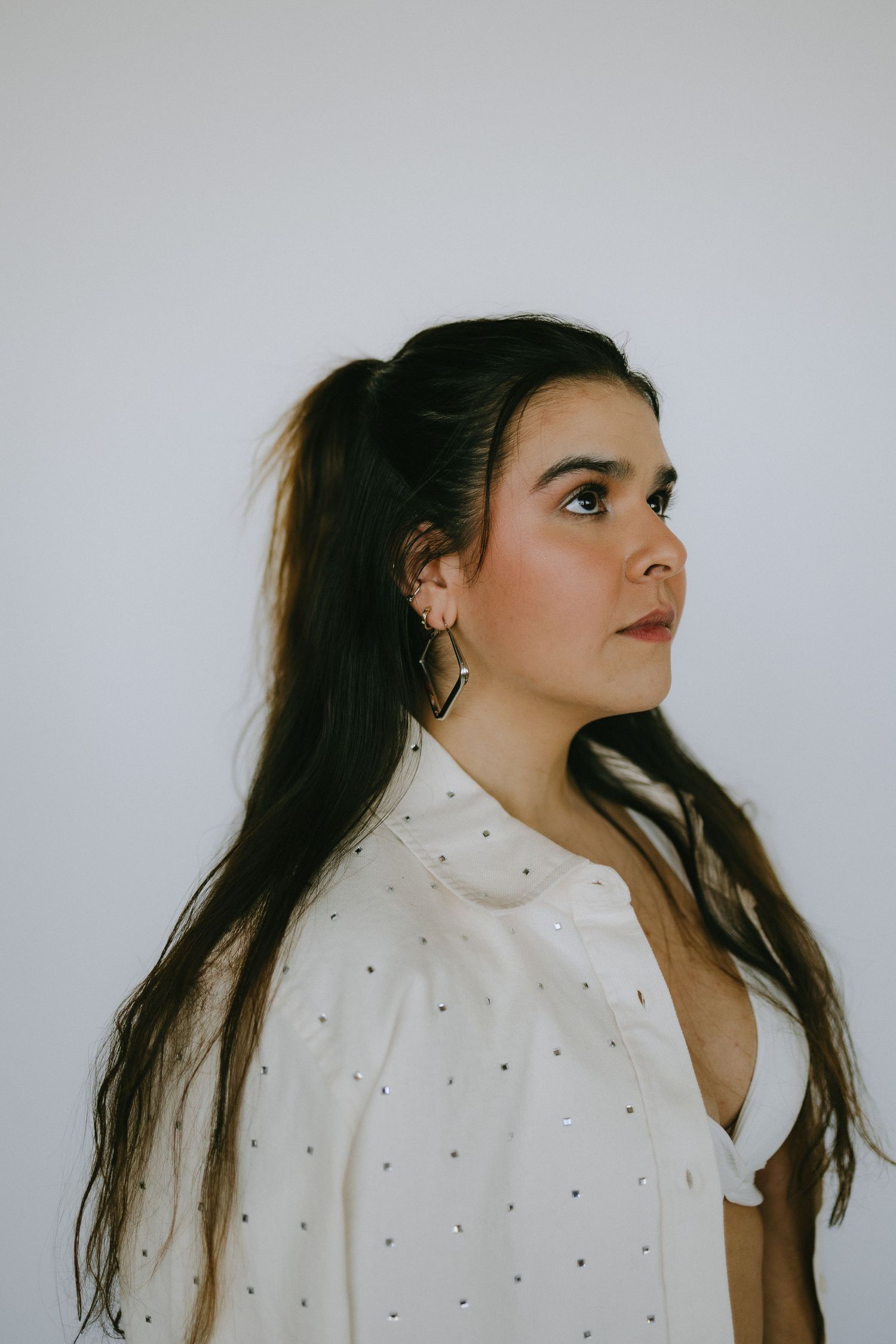 Side profile portrait in white studded jacket against neutral background.
