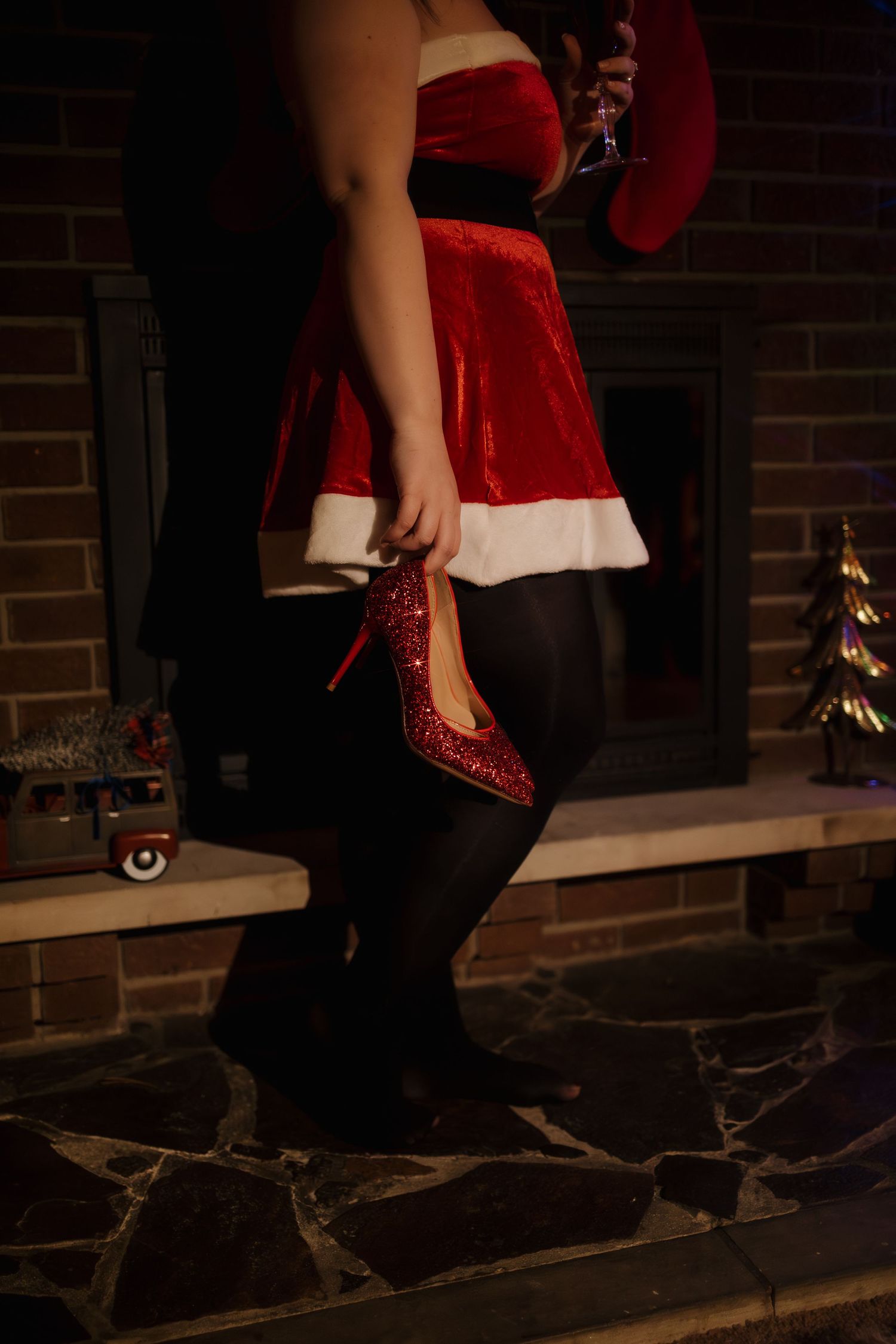 Festive red Santa dress with glittery heels against brick fireplace backdrop.