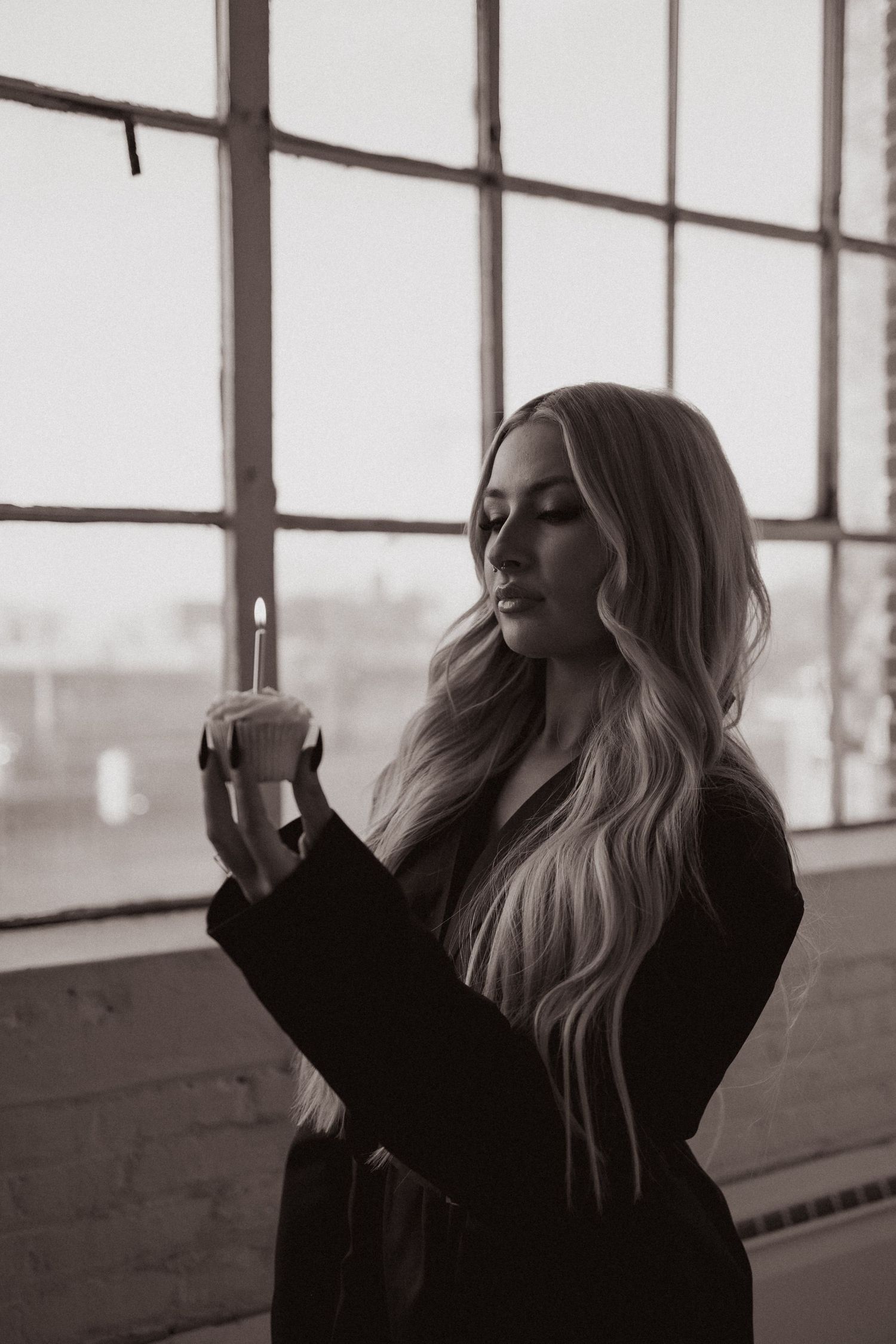 Moody black and white portrait by industrial window holding candle.