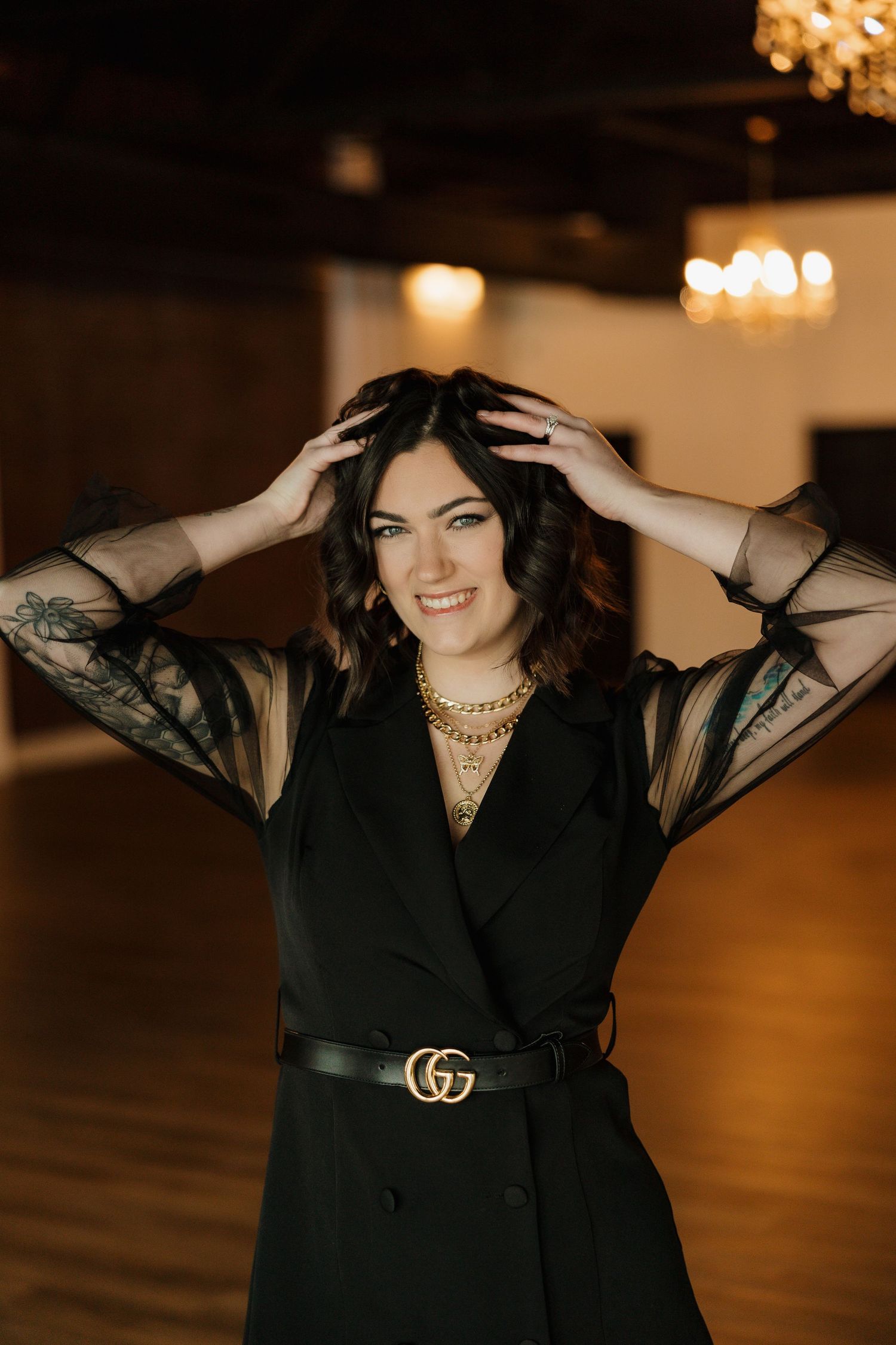 Fashion portrait in a black dress with sheer sleeves and Gucci belt in an elegant indoor setting.