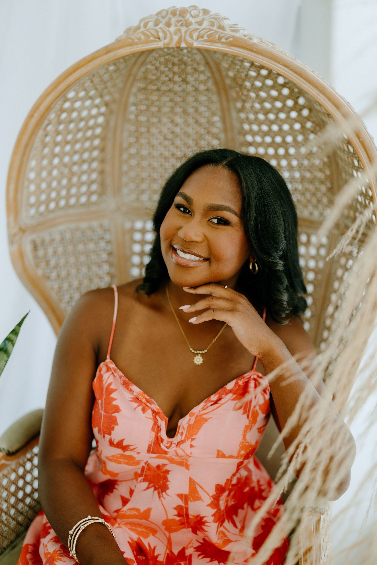 Elegant portrait seated in peacock chair wearing coral floral dress.