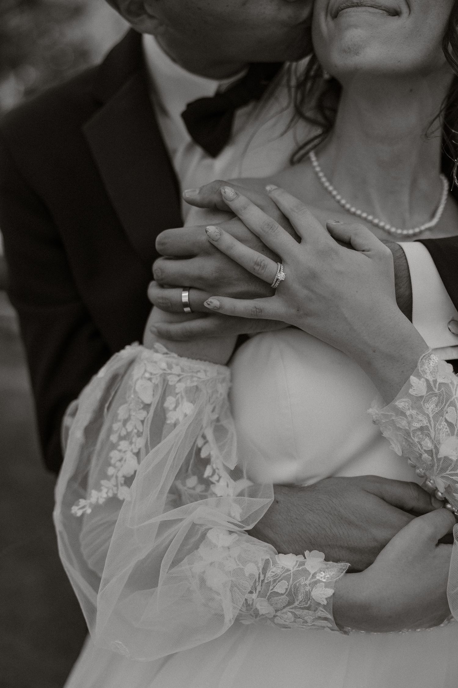 Black and white close-up of hands gently touching a lace wedding dress.